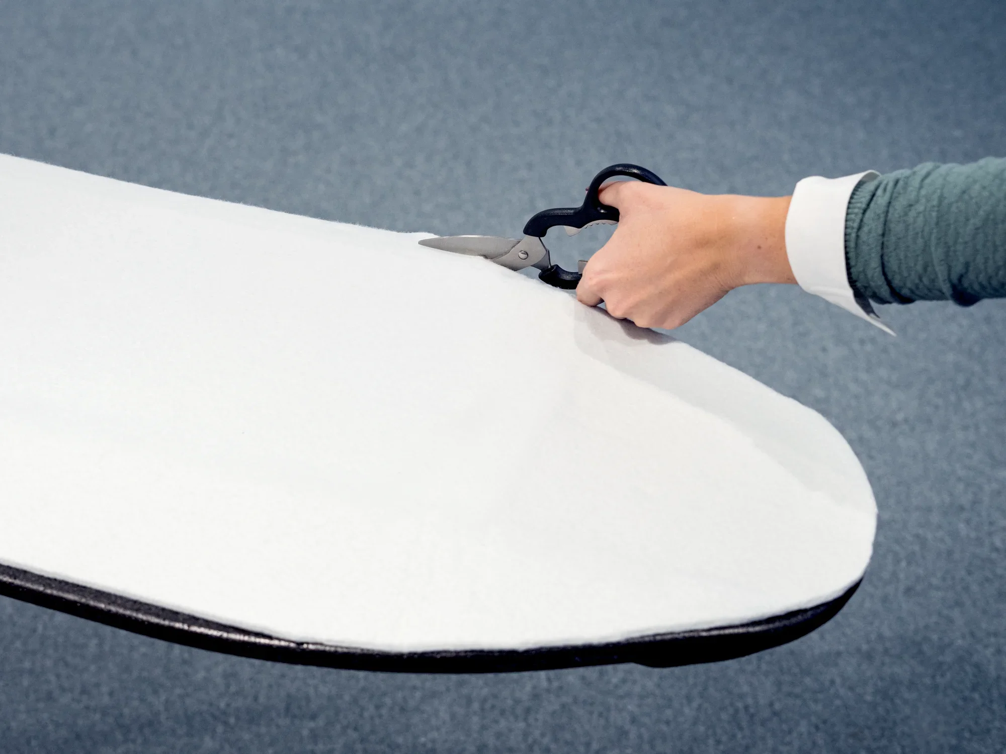 Una persona corta con unas tijeras el acolchado de la tabla de planchar. El acolchado blanco se corta con precisión para que se adapte perfectamente a la tabla de planchar.