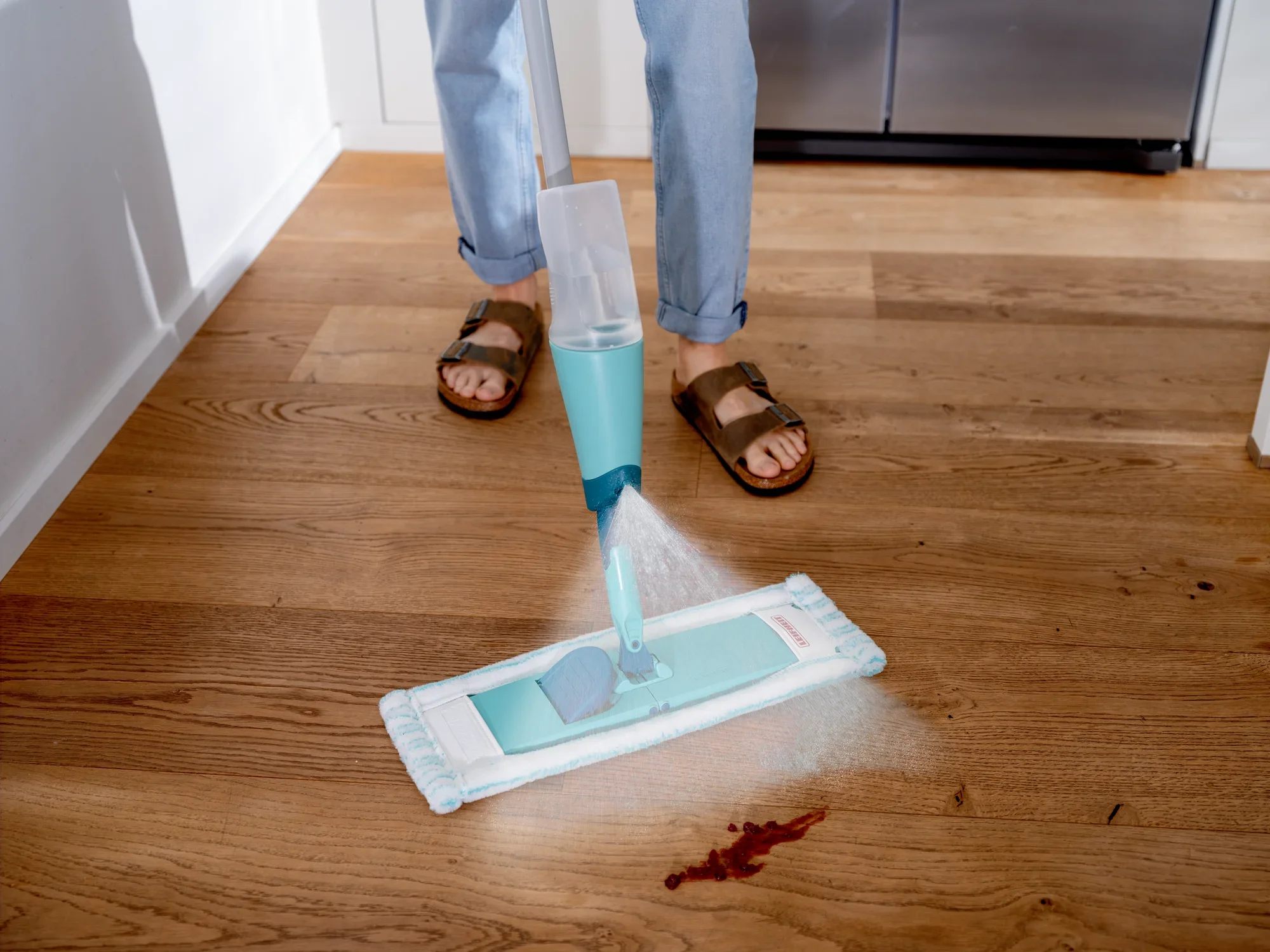 Ein Sprühwischer Easy Spray XL wird auf einem Holzboden verwendet, um einen kleinen Fleck zu reinigen. Der Wischer sprüht Wasser vor sich, während eine Person ihn bedient.