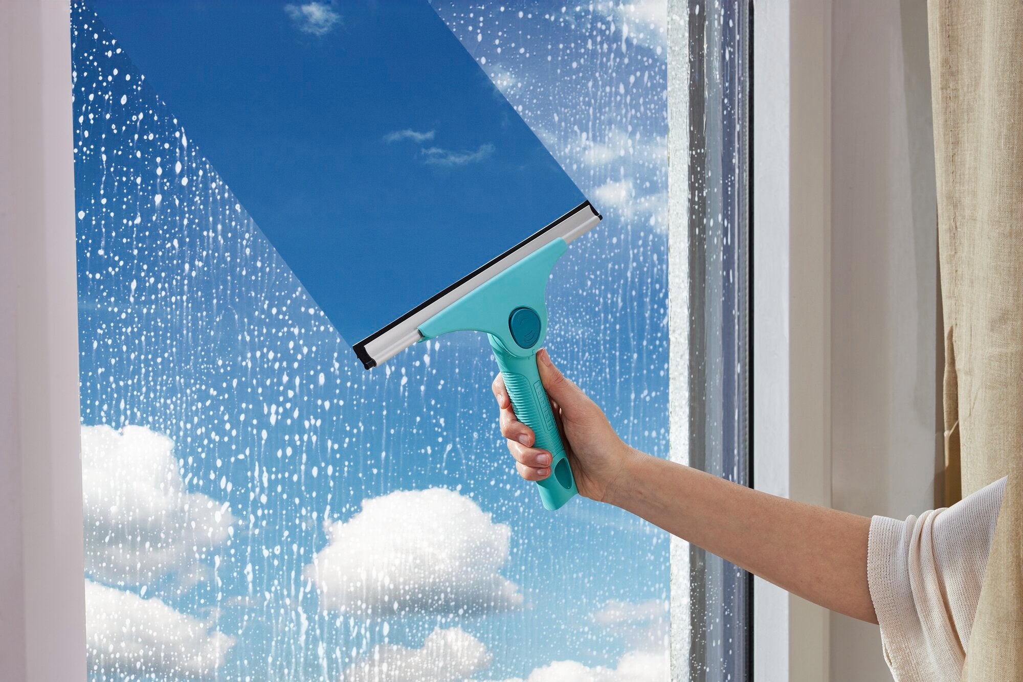 Ein Fensterreiniger namens "Window Slider 2in1 M ProReach" wird verwendet, um ein großes Fenster zu reinigen. Der blaue Himmel und Wolken sind durch das klare Glas sichtbar.