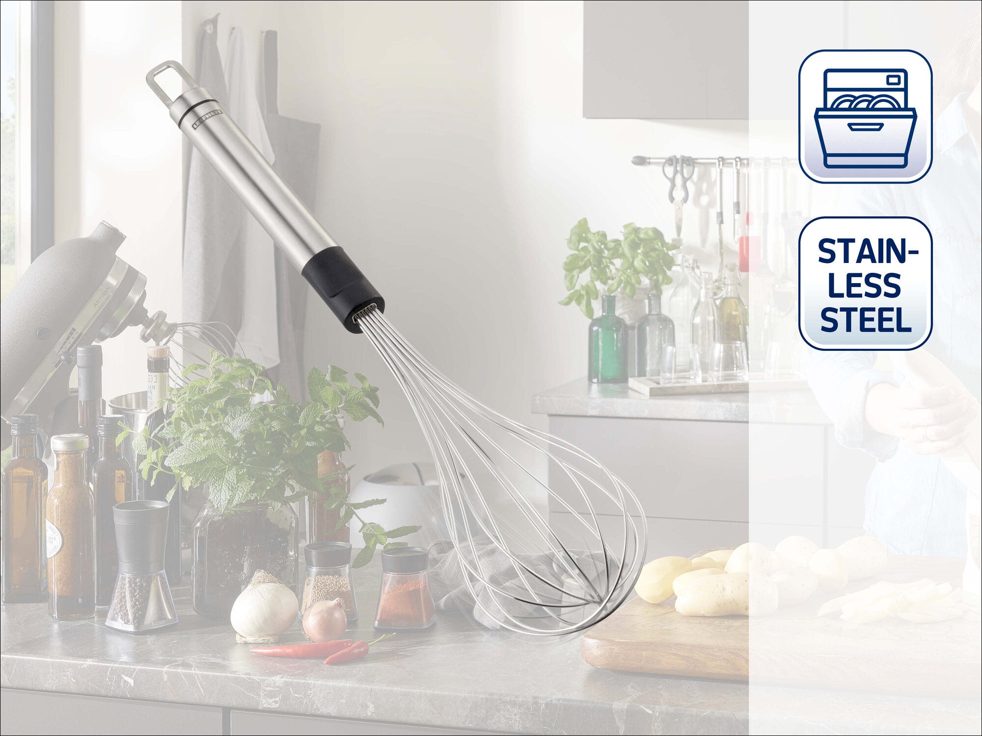 Leifheit Schneebesen Sterling aus Edelstahl mit schlankem Griff und Drahtschlaufen, schräg auf einer Küchenarbeitsplatte vor Kräutern, Gewürzen und modernem Küchenhintergrund platziert.