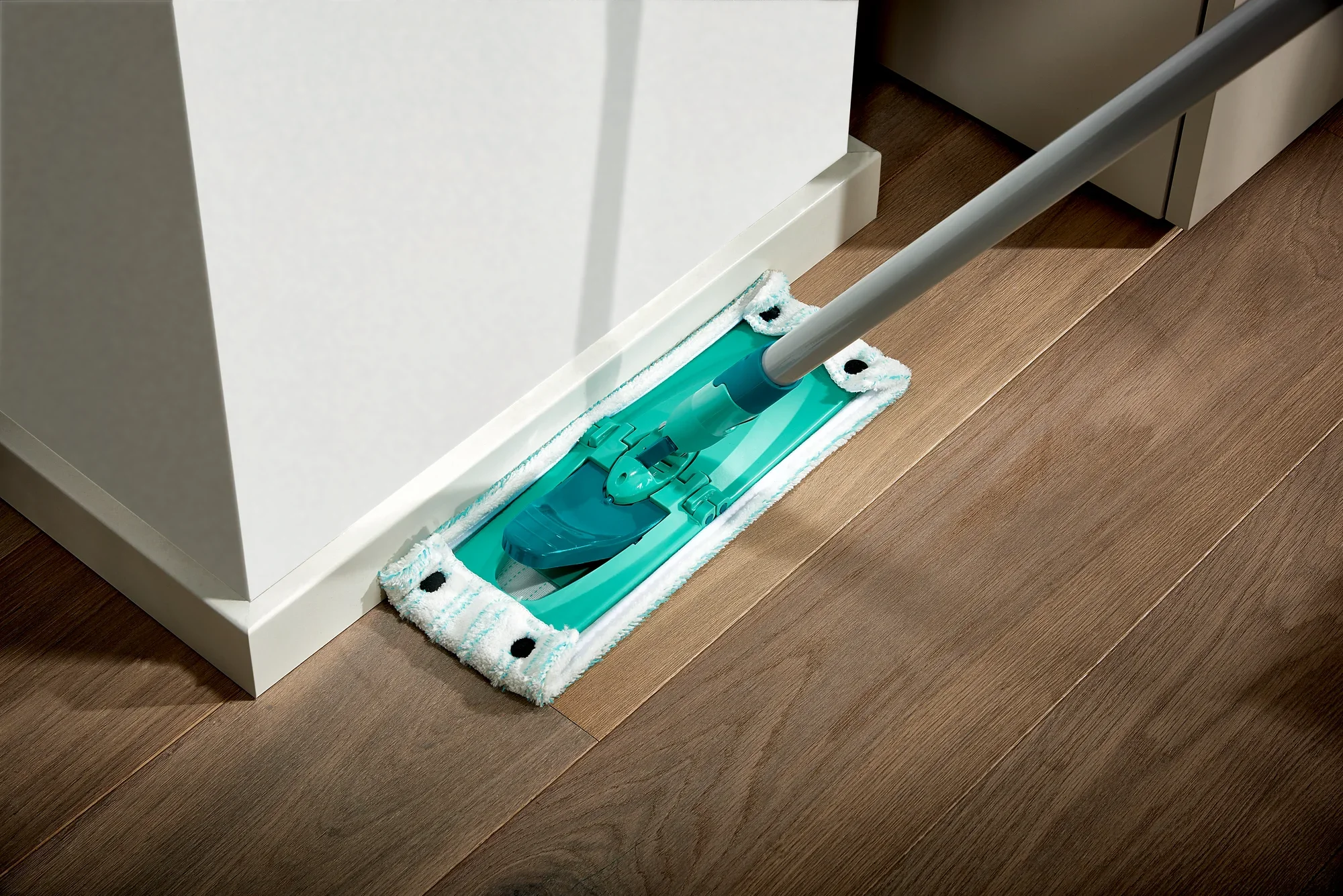 A floor mop from the Combi M series is used to clean the floor along a wall. The mop has a flat, rectangular design and is ideal for corners.