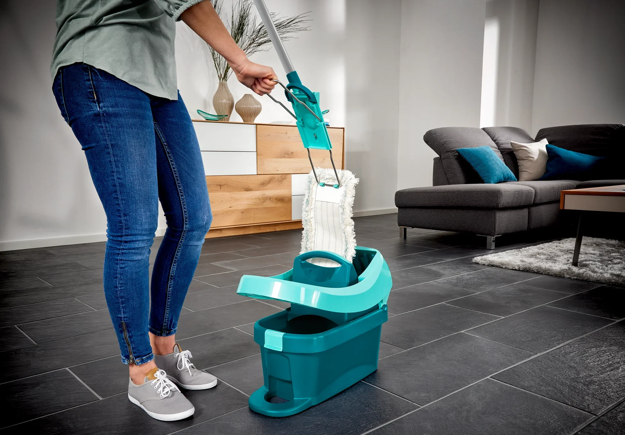 Eine Person verwendet den Bodenwischer Profi XL in einem modernen Wohnzimmer. Der Wischer hat einen Baumwollkopf und ist in einem Eimer mit Auswringmechanismus platziert. Ideal für gründliche Reinigung.