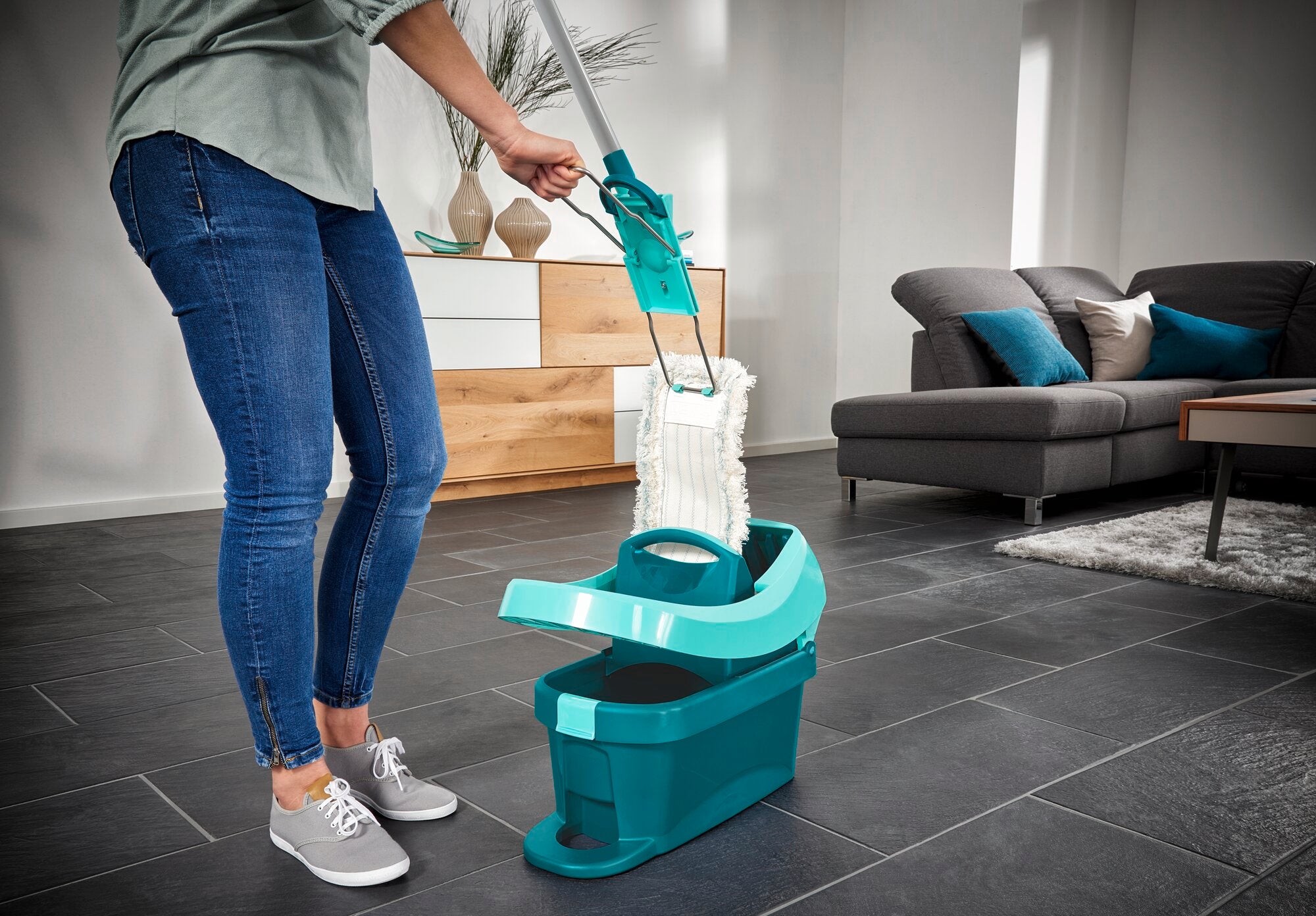 Osoba używa mopa Profi XL w nowoczesnym salonie. Mop ma bawełnianą nakładkę i jest umieszczony w wiadrze z mechanizmem wyżymającym. Idealny do dokładnego czyszczenia.