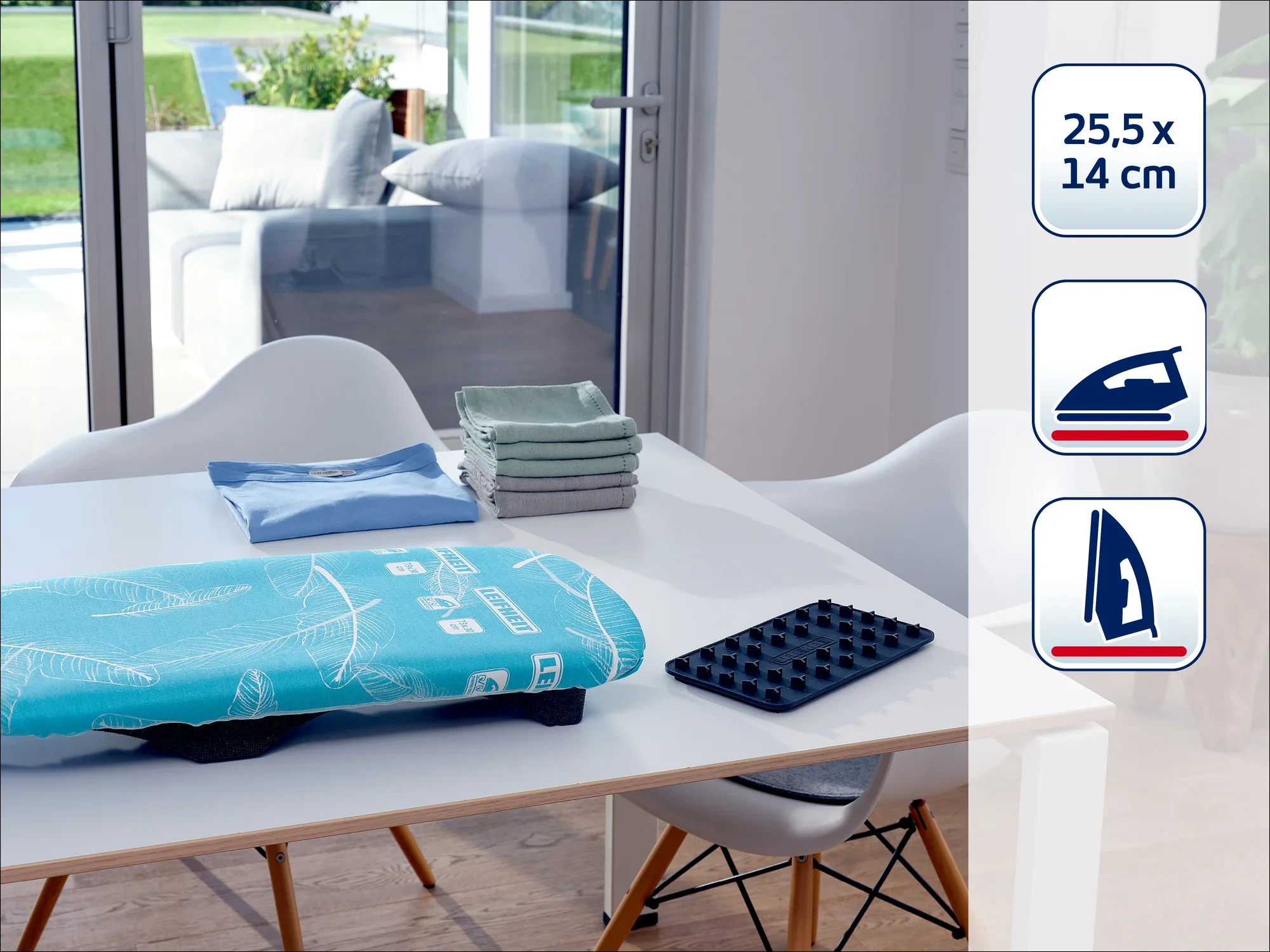 Une table à repasser moderne avec des accessoires, dont une planche à repasser bleue, un tapis pour fer à repasser noir et des serviettes pliées. À l'arrière-plan, une pièce lumineuse avec de grandes fenêtres.