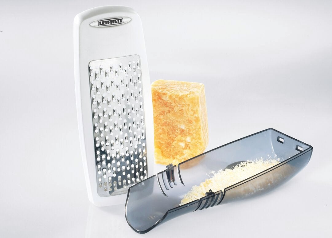 Une râpe à parmesan Leifheit à côté d'un morceau de parmesan et d'un bol de fromage râpé. La râpe a un design moderne et est idéale pour la cuisine.