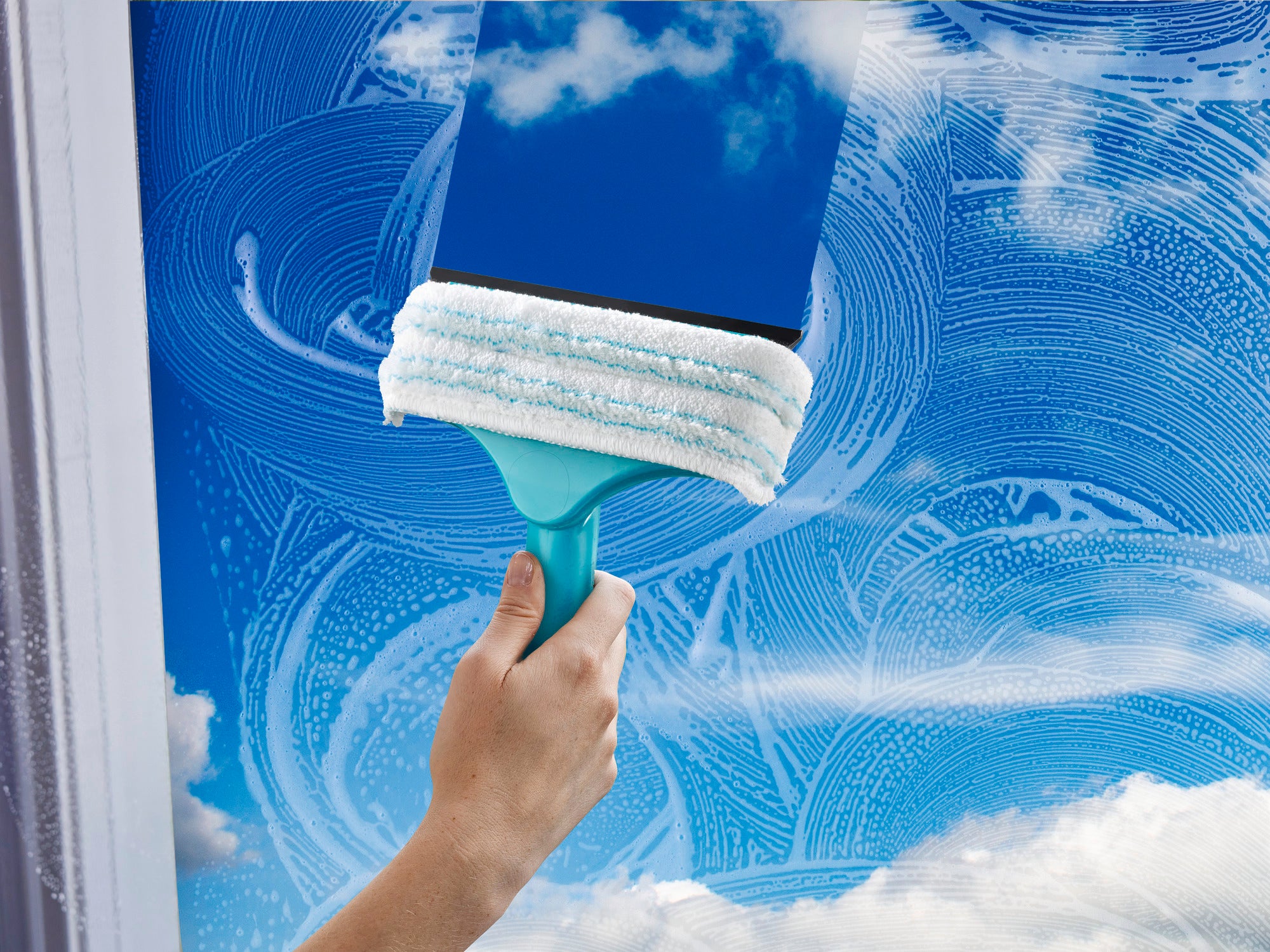 Een 3-in-1 mini raam- en kozijnwisser wordt gebruikt om een raam schoon te maken. De wisser heeft een turquoise gekleurd handvat en een wit reinigingsdoekje. De lucht wordt weerspiegeld in het schone glas.