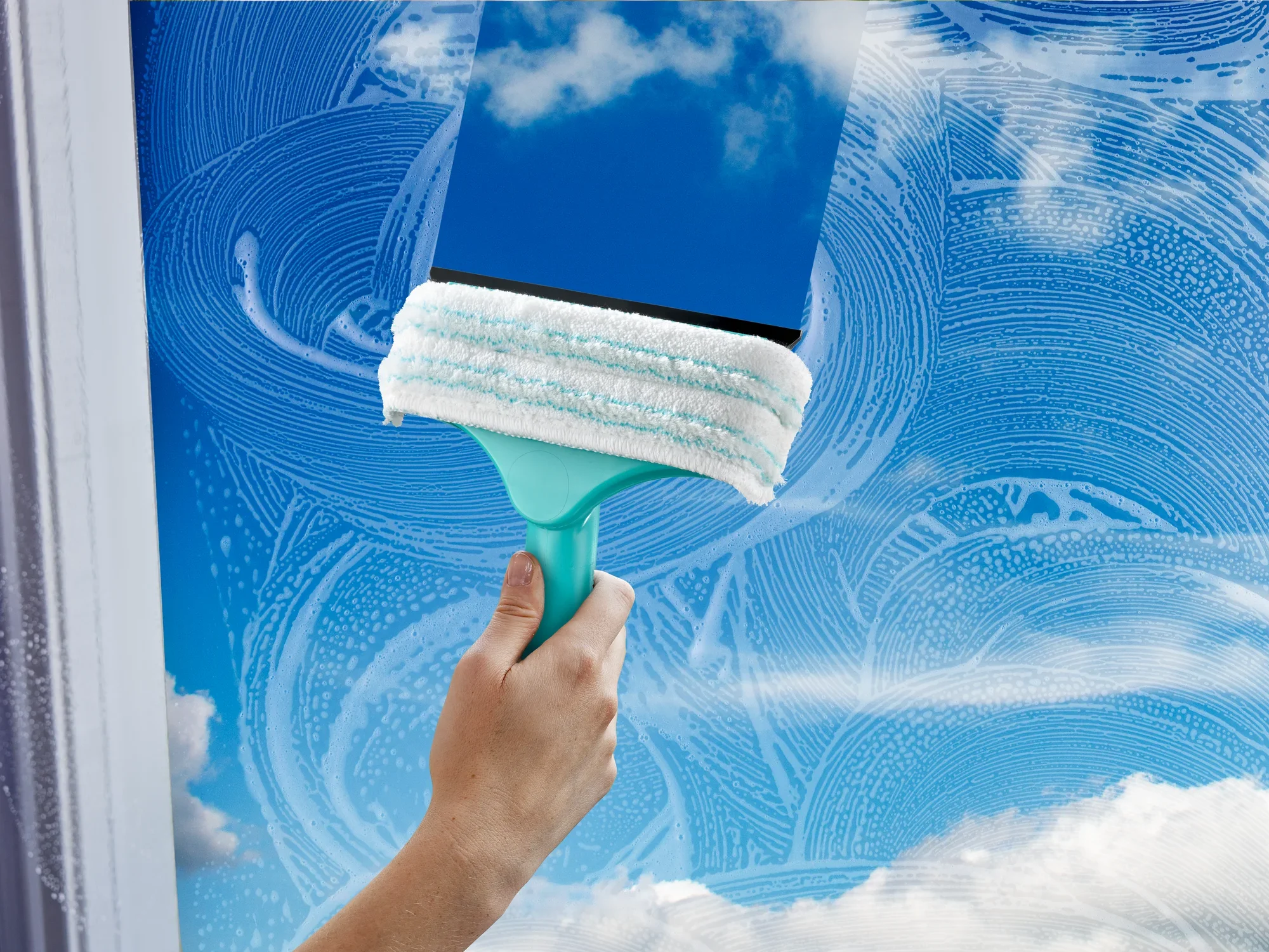 Mini ściągaczka do okien i ram 3 w 1 służy do czyszczenia okien. Wycieraczka ma uchwyt w kolorze turkusowym i białą nakładkę czyszczącą. W czystej szybie odbija się niebo.
