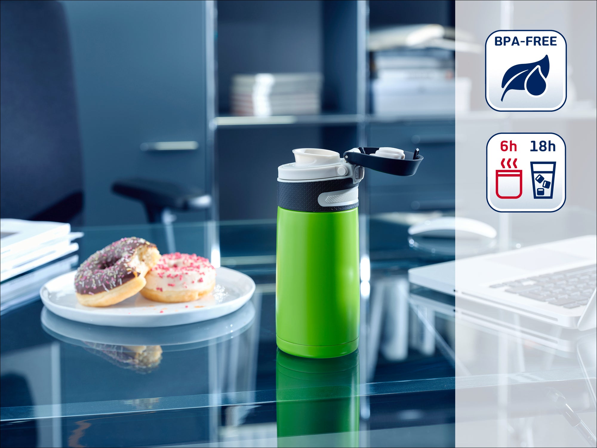 Une bouteille thermos verte est posée sur une table en verre dans un bureau. À côté, deux beignets sont disposés sur une assiette. La bouteille est sans BPA et garde les boissons chaudes pendant 6 heures et froides pendant 18 heures.
