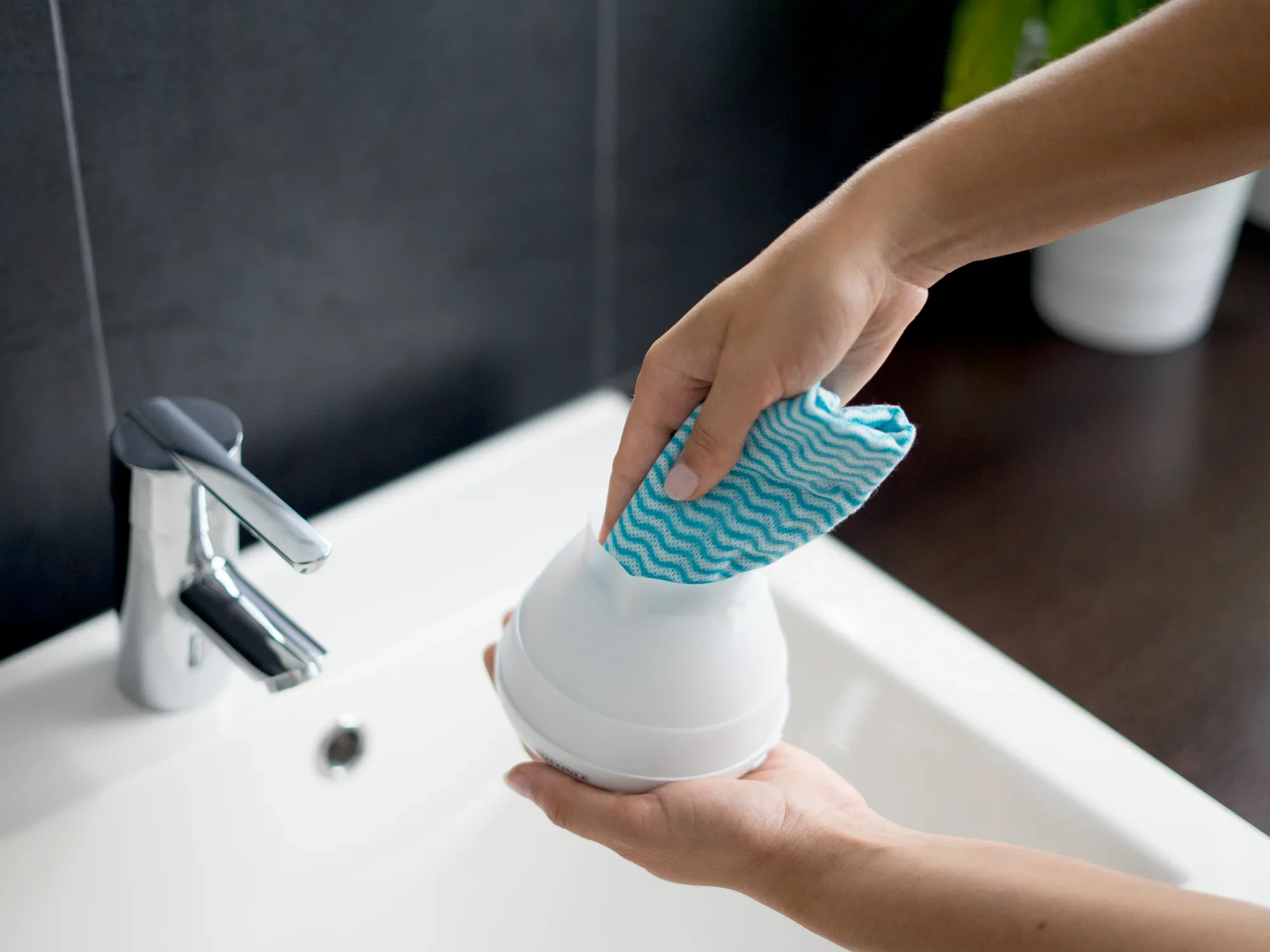 Une personne nettoie le diffuseur d'arômes design Bari avec un chiffon bleu au-dessus d'un lavabo. Le diffuseur a une surface lisse et blanche et est soigneusement essuyé.
