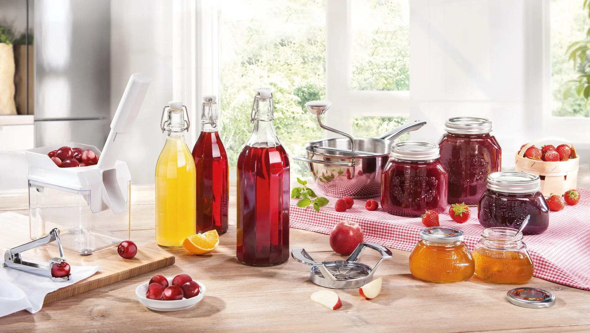 Een Leifheit kersenpitter staat op een tafel omringd door potten kersenjam, flessen sap en verse kersen. Op de achtergrond is een lichtgekleurde keuken te zien.