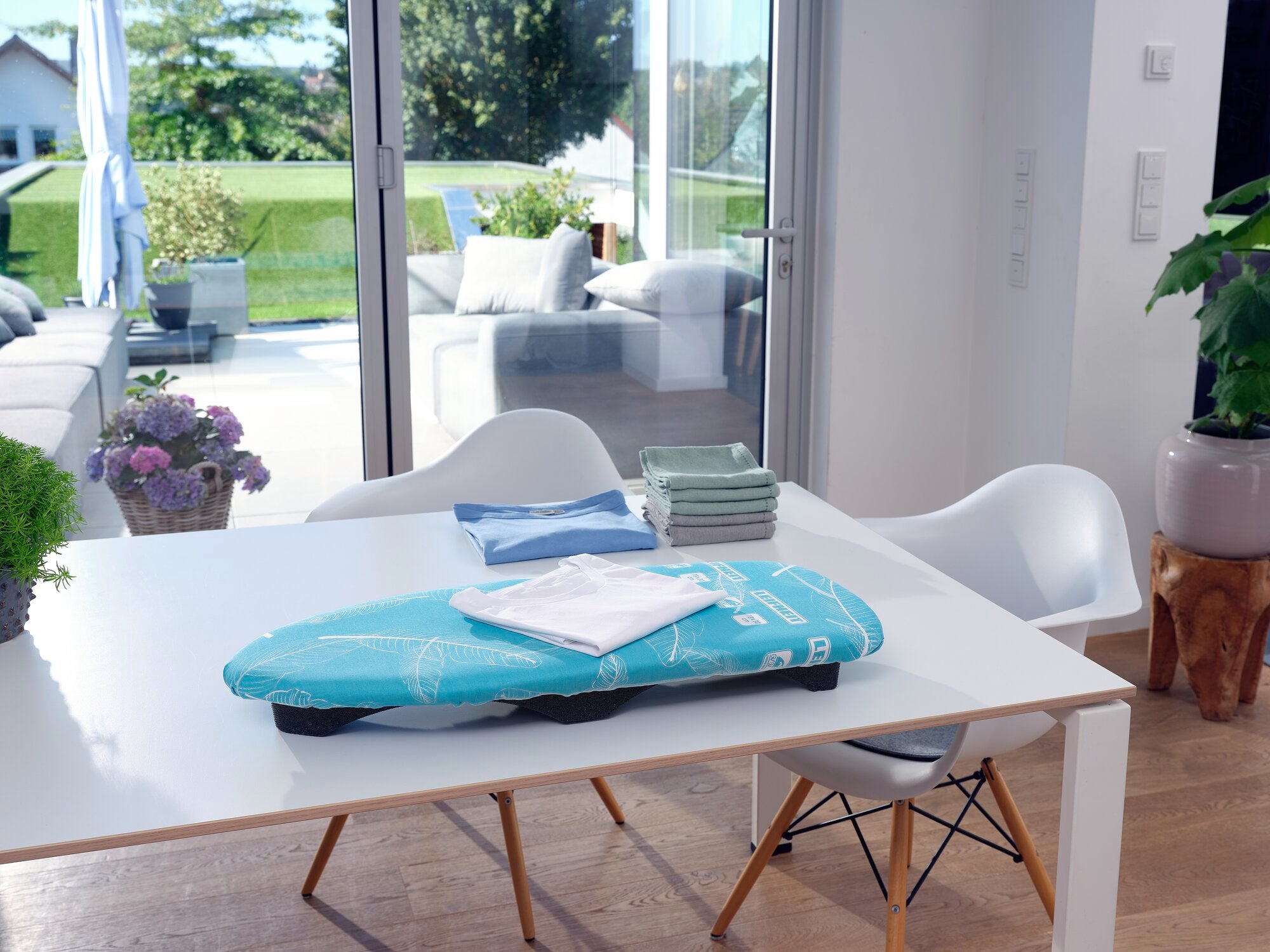 Een compacte strijkplank, de Air Board Table Compact, rust op een moderne eettafel in een lichte kamer met uitzicht op een zonnig terras.