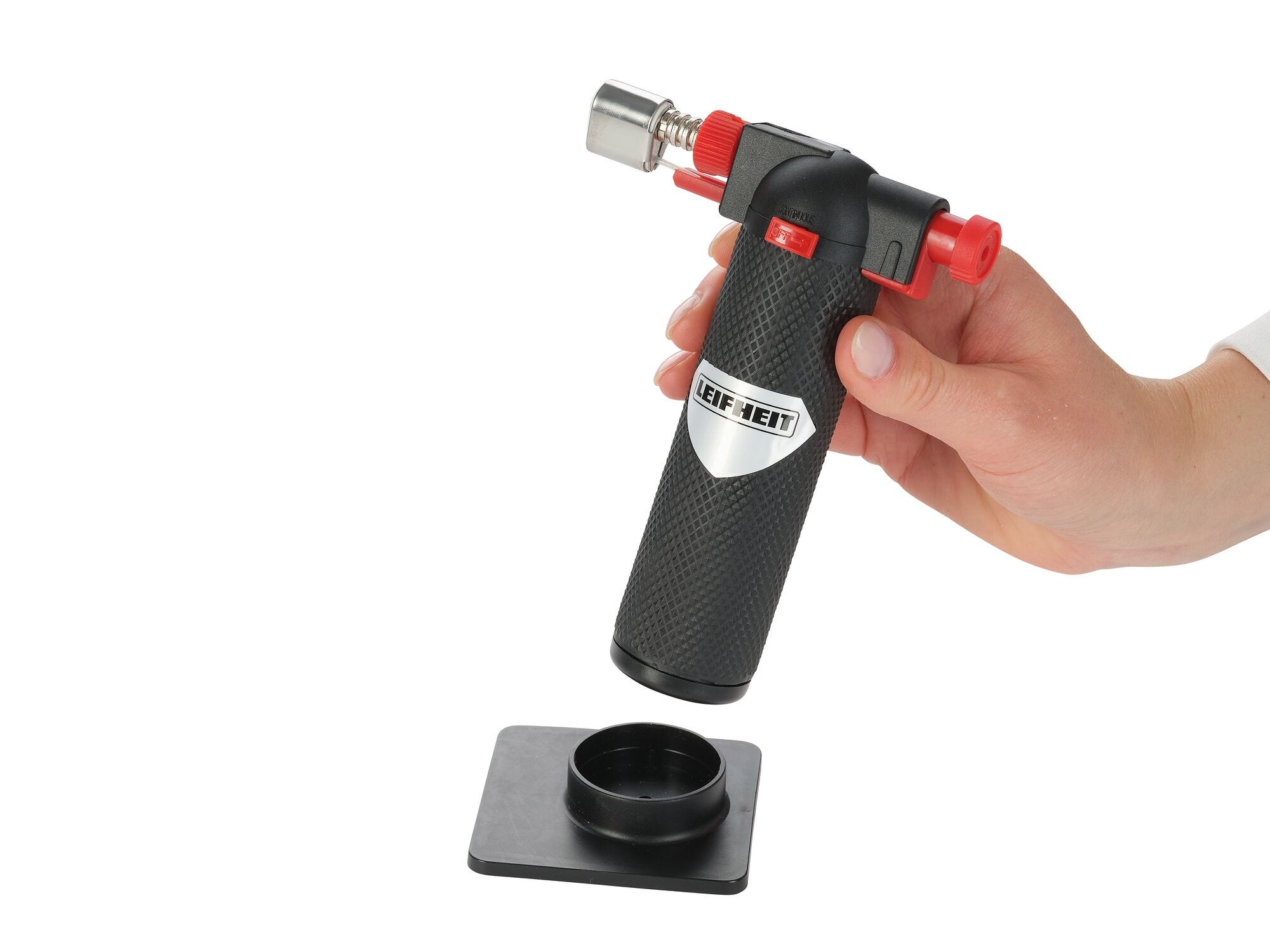 Een flammkuip van het merk Leifheit wordt met één hand vastgehouden. Het zwarte handvat is gestructureerd en de branderkop is zilverkleurig met rode accenten. Ideaal voor het karamelliseren van desserts.