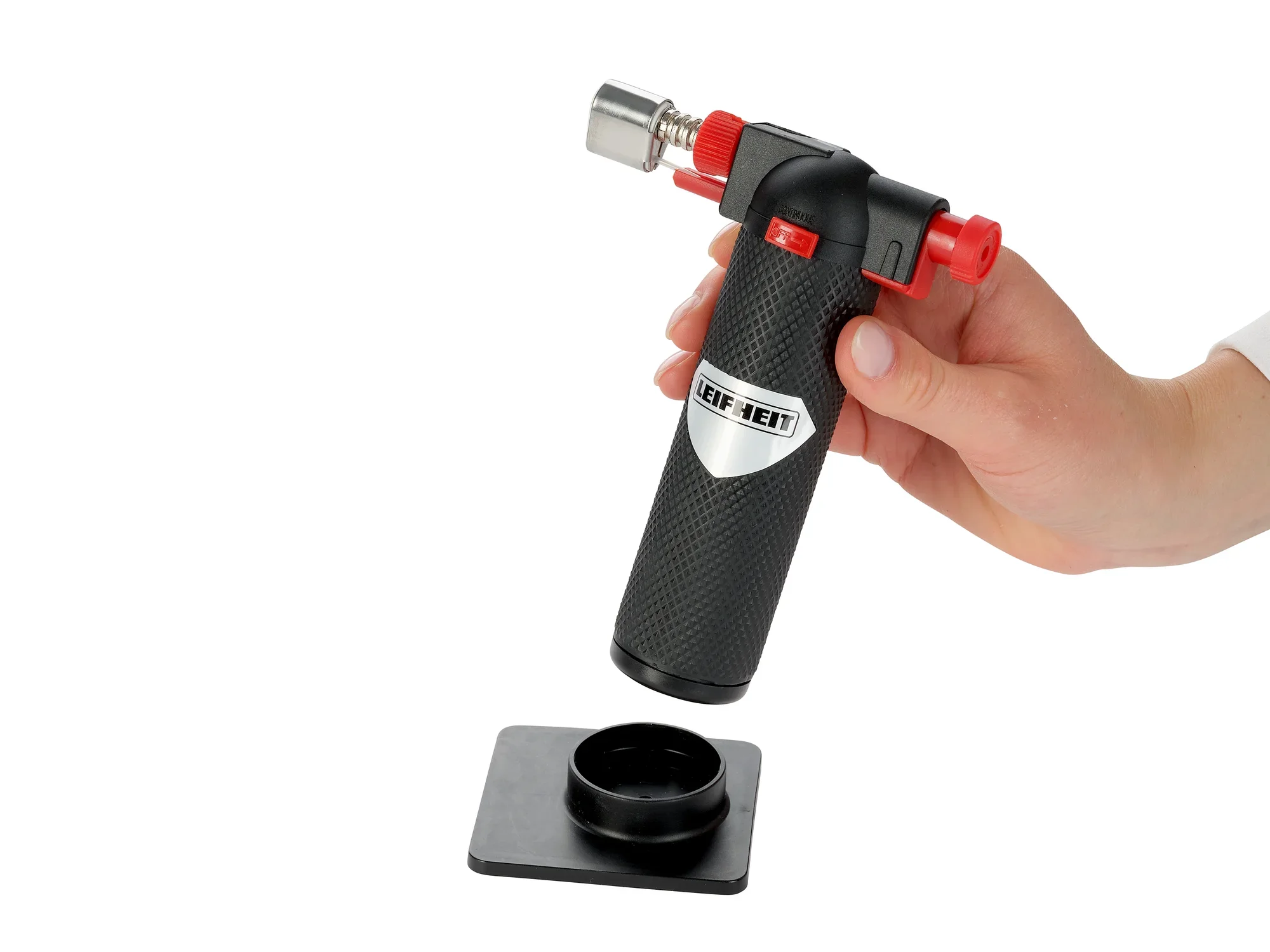 Ein Flambierer der Marke Leifheit wird von einer Hand gehalten. Der schwarze Griff ist strukturiert, und der Brennerkopf ist silbern mit roten Akzenten. Ideal zum Karamellisieren von Desserts.