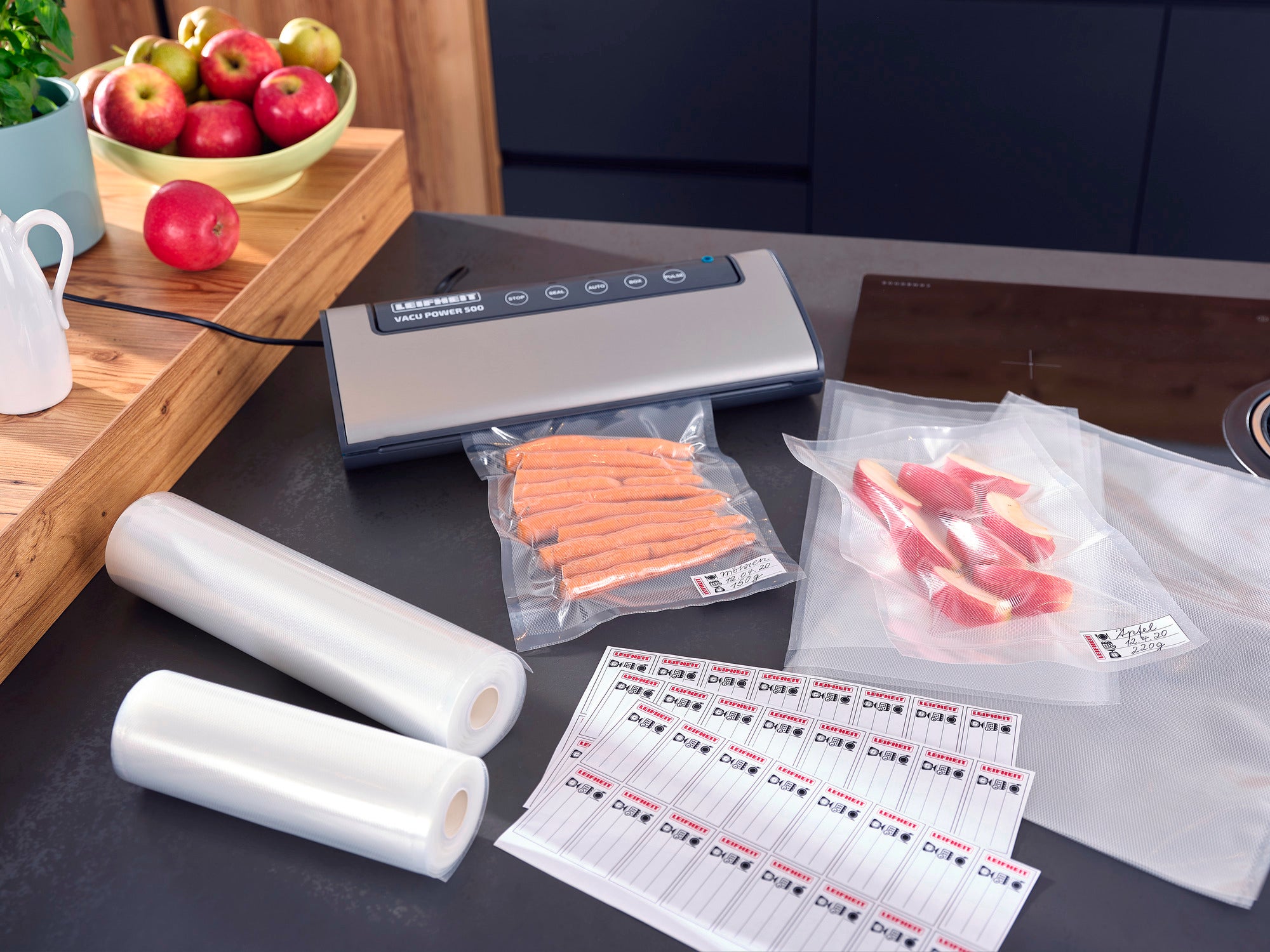 Vacuum bags 20x30cm on a kitchen table with a vacuum sealer, two rolls of vacuum film, vacuum-packed food and labels. Ideal for keeping food fresh.