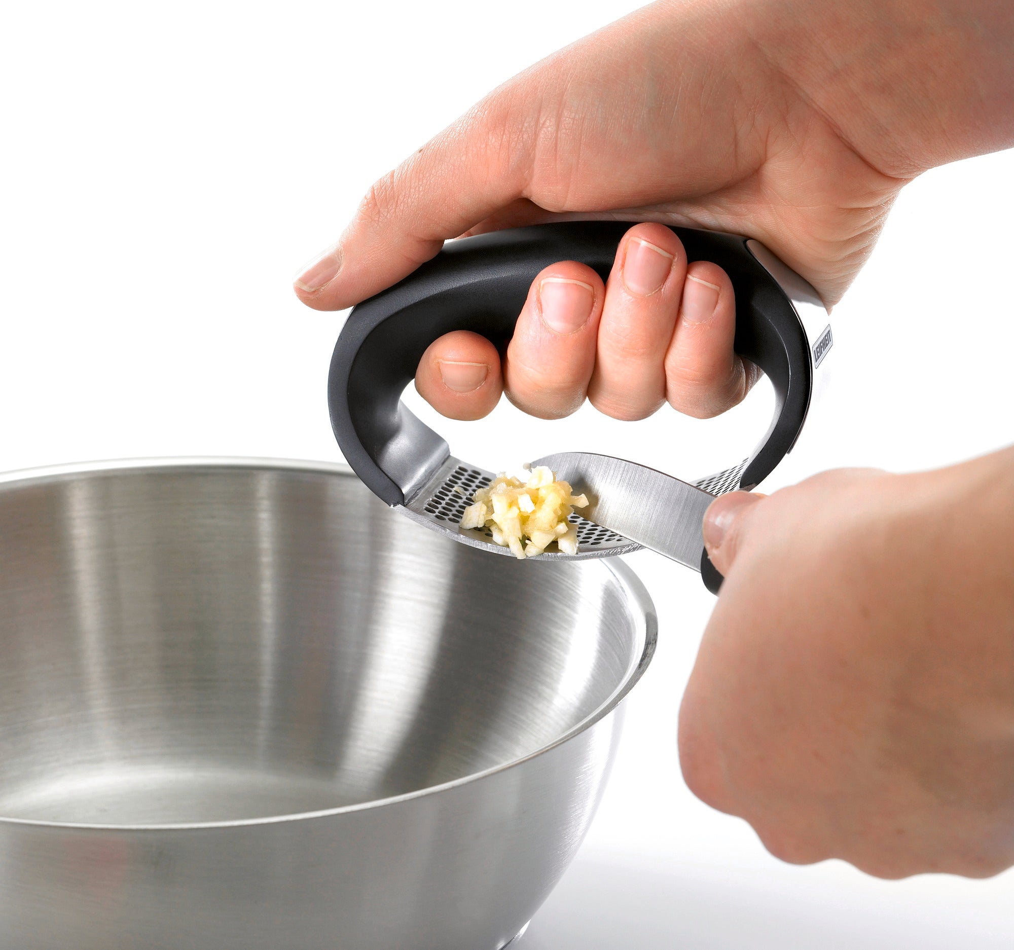 One hand uses the Knobi King garlic press to press fresh garlic into a metal bowl. The ergonomic shape makes pressing easy without much effort.