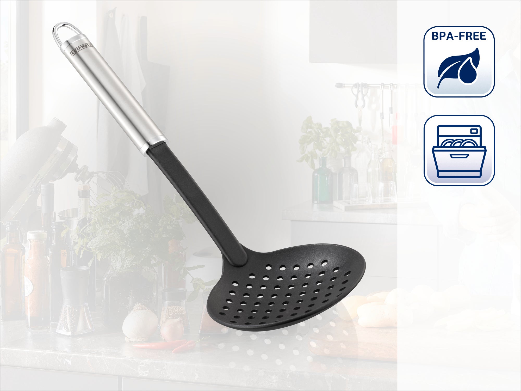Utensilio de cocina con cuchara negra perforada y mango plateado. Ideal para escurrir alimentos. Sin BPA y apto para lavavajillas. Con una cocina moderna de fondo.