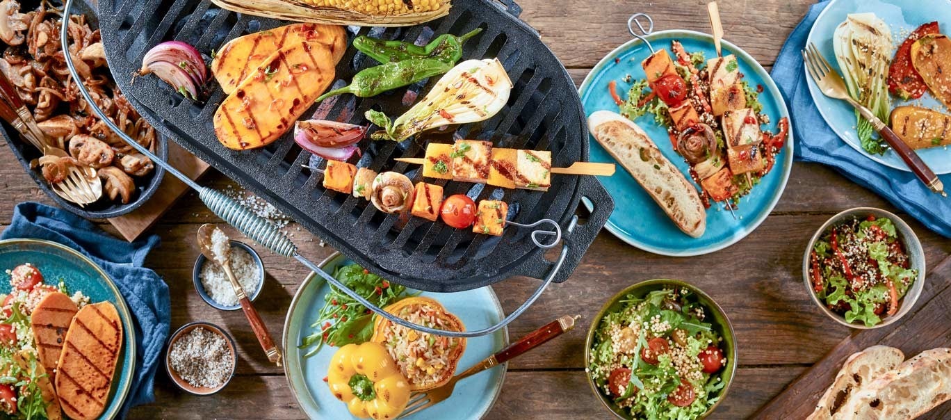 Gegrilltes Gemuese und Spiesse auf einem Tisch, umgeben von Salaten, Brot und Gewuerzen, bieten ein buntes und leckeres BBQ-Fest.