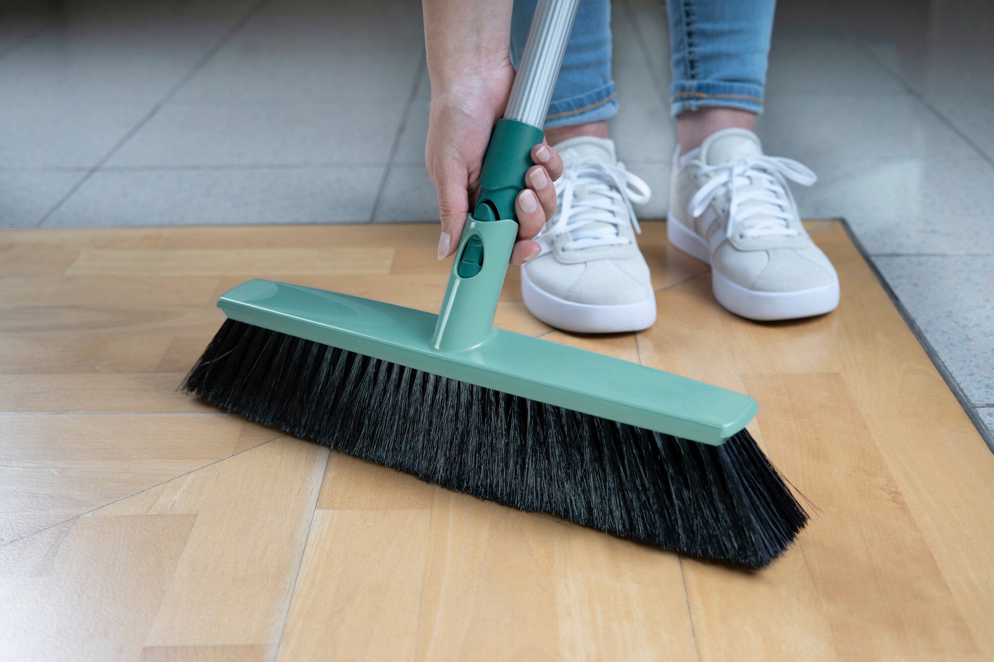 Une personne tient le balai polyvalent Xtra Clean d'une largeur de 40 cm. Le balai a des poils noirs et un manche vert, idéal pour nettoyer les sols.