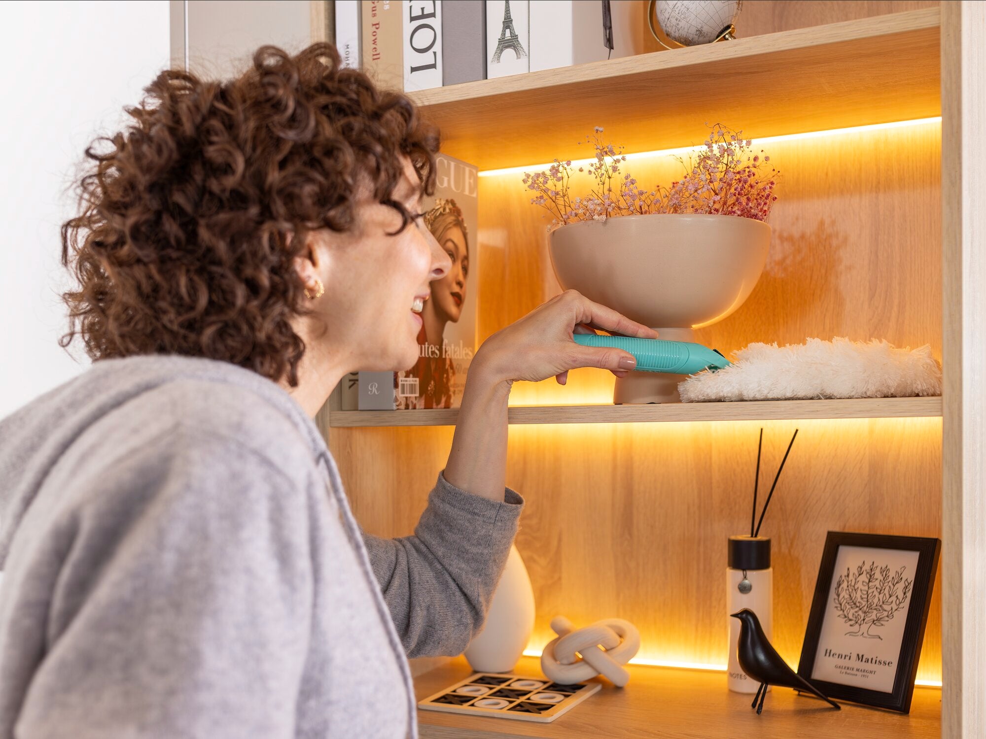 Een persoon gebruikt de SUPERDUSTER plumeau om een plank schoon te maken. De plumeau bereikt moeiteloos de moeilijk bereikbare plaatsen en zorgt voor een grondige reiniging.