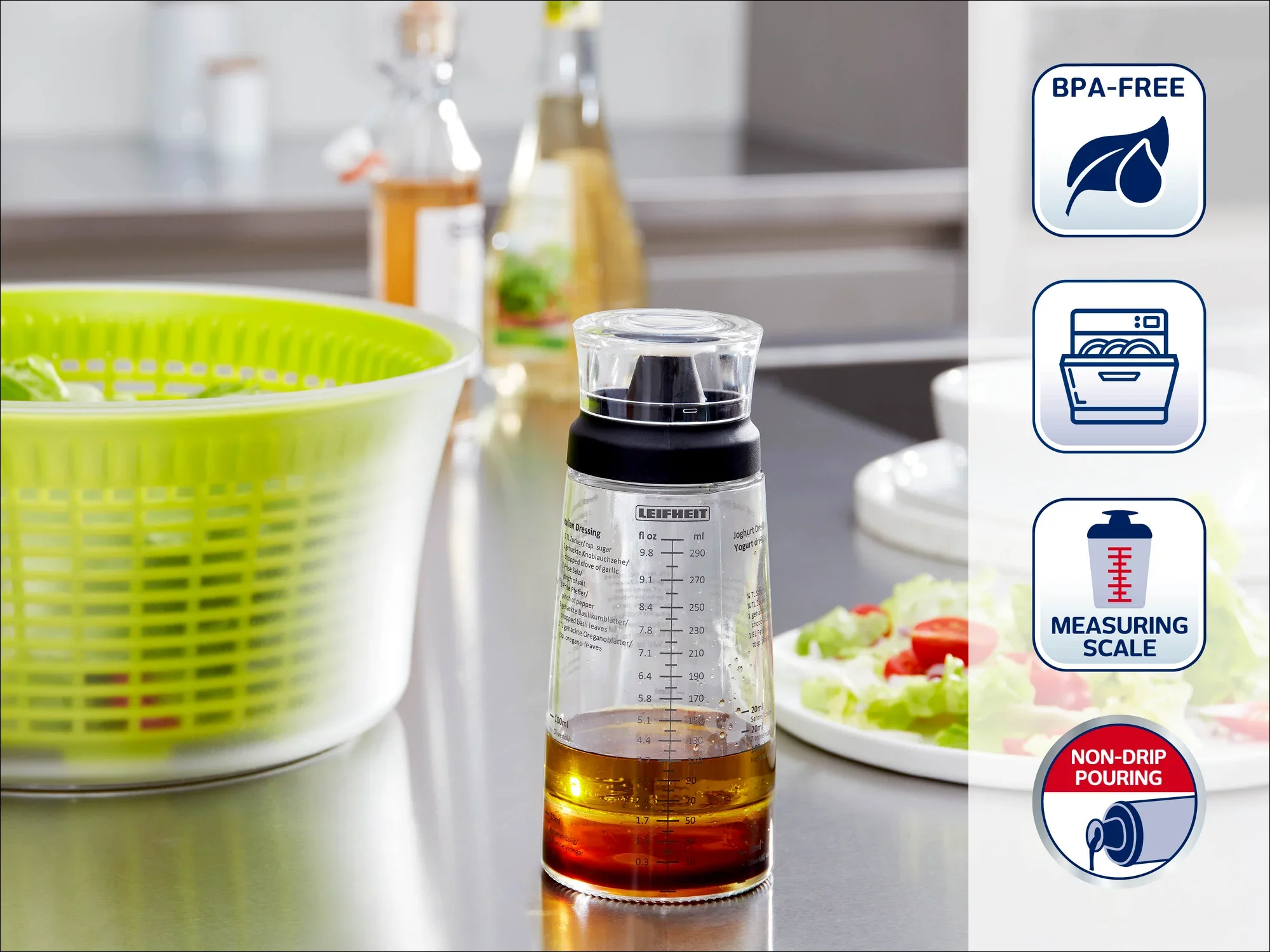 Een transparante maatbeker met een zwart deksel staat op een keukenblad. Er staat een maatverdeling op en het is BPA-vrij. Op de achtergrond zijn een slacentrifuge en verse ingrediënten te zien.