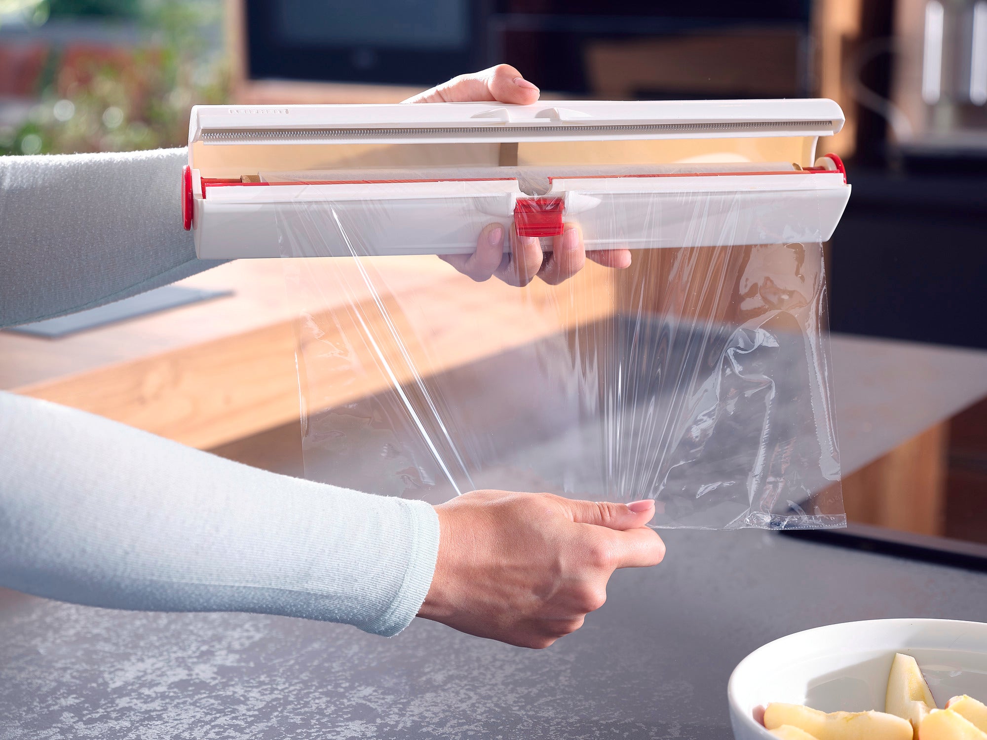 Eine Person benutzt den Folienschneider Perfect Cut, um Frischhaltefolie präzise abzuschneiden. Der Schneider hat ein modernes Design und erleichtert das Abtrennen der Folie.