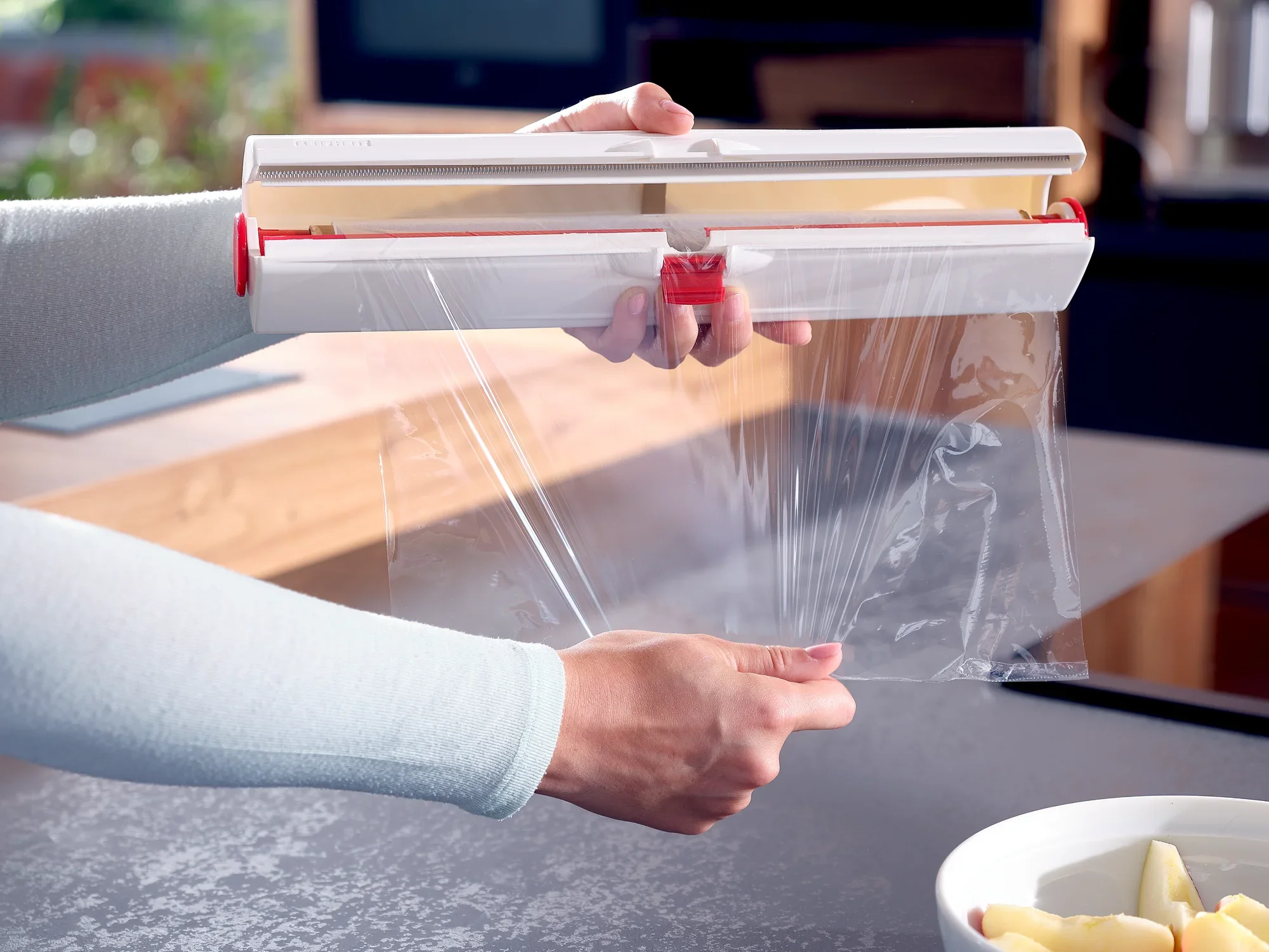 A person is using the Perfect Cut foil cutter to cut cling film precisely. The cutter has a modern design and makes it easy to cut the foil.