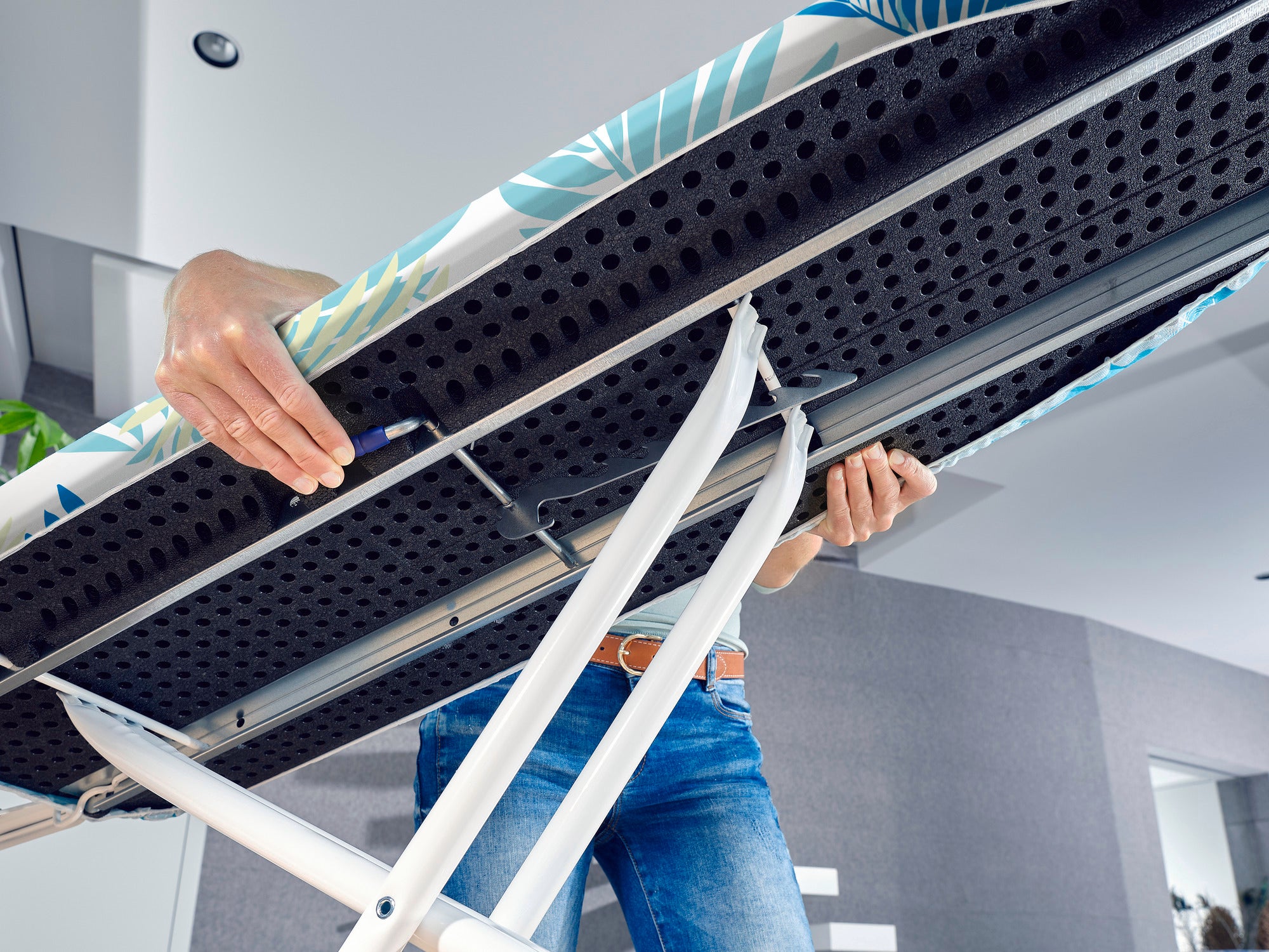 Bügelbrett Air Board M Compact Plus Jungle: Nahaufnahme einer Person, die das Bügelbrett verstellt. Das Design zeigt tropische Blätter, die Stabilität und Stil vereinen.