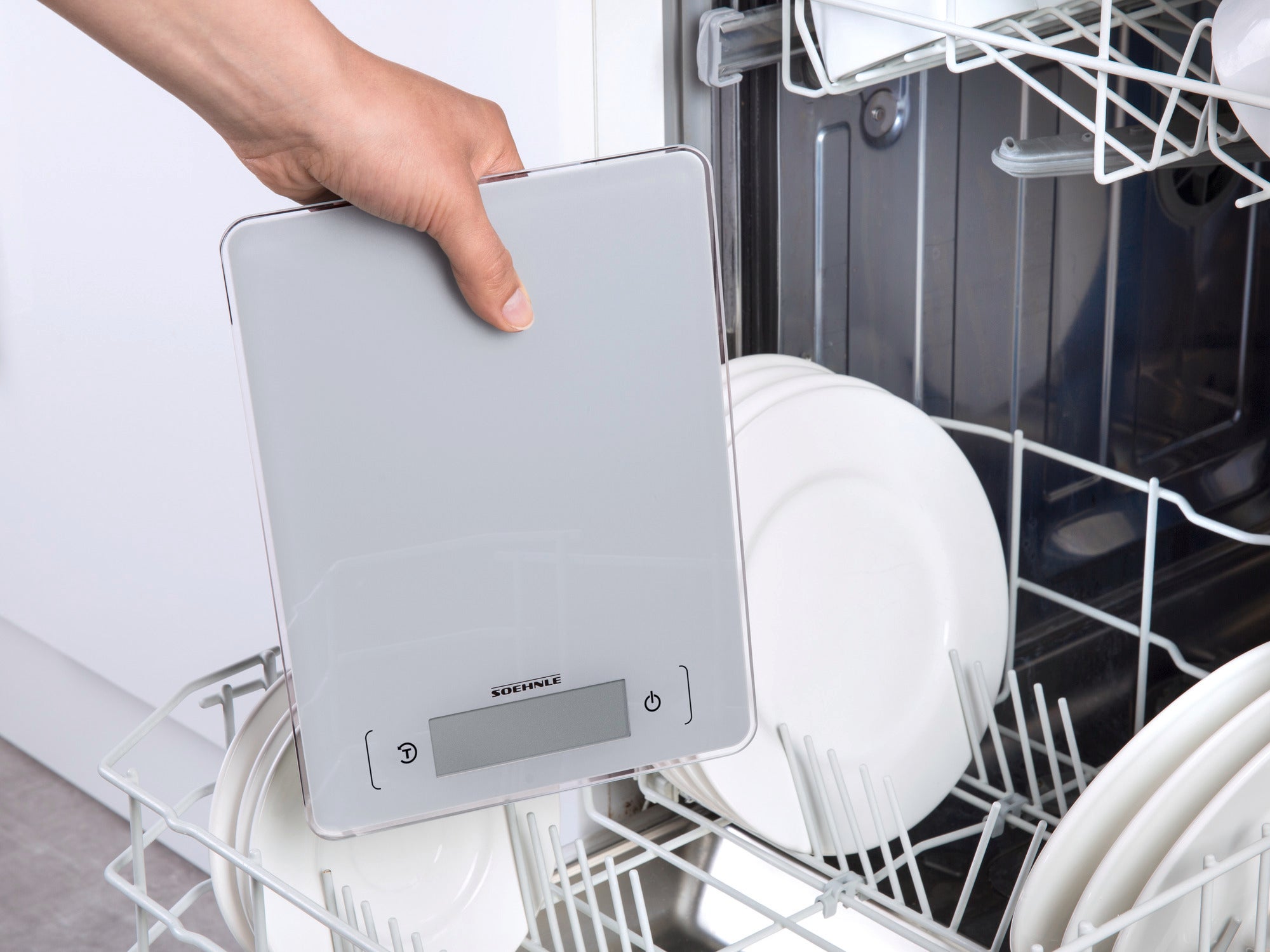 Eine digitale Küchenwaage wird aus einem Geschirrspüler entnommen. Die Waage ist flach und hat ein modernes Design mit einem klaren Display. Ideal für präzises Wiegen in der Küche.
