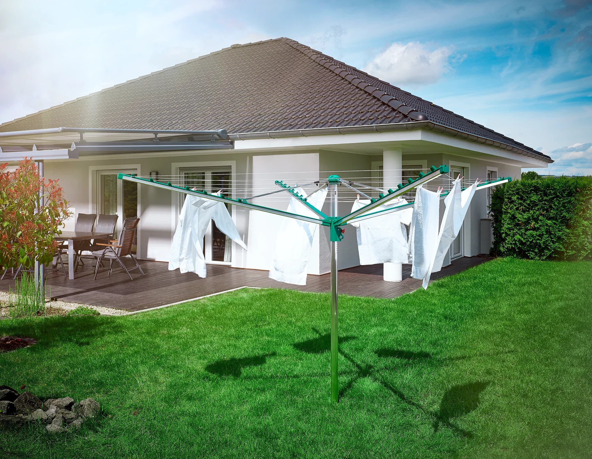 Séchoir à linge Linomatic 400 Comfort dans le jardin devant une maison moderne. Le séchoir à linge est recouvert de draps blancs et se trouve sur une pelouse verte bien entretenue.