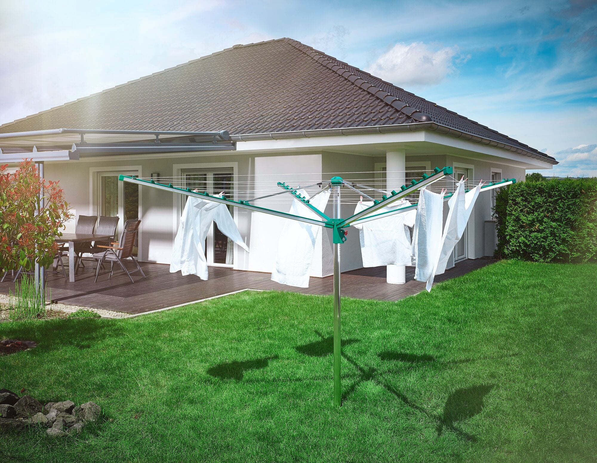 Wäschespinne Linomatic 400 Comfort im Garten vor einem modernen Haus. Die Wäschespinne ist mit weißen Laken behängt und steht auf einem gepflegten, grünen Rasen.