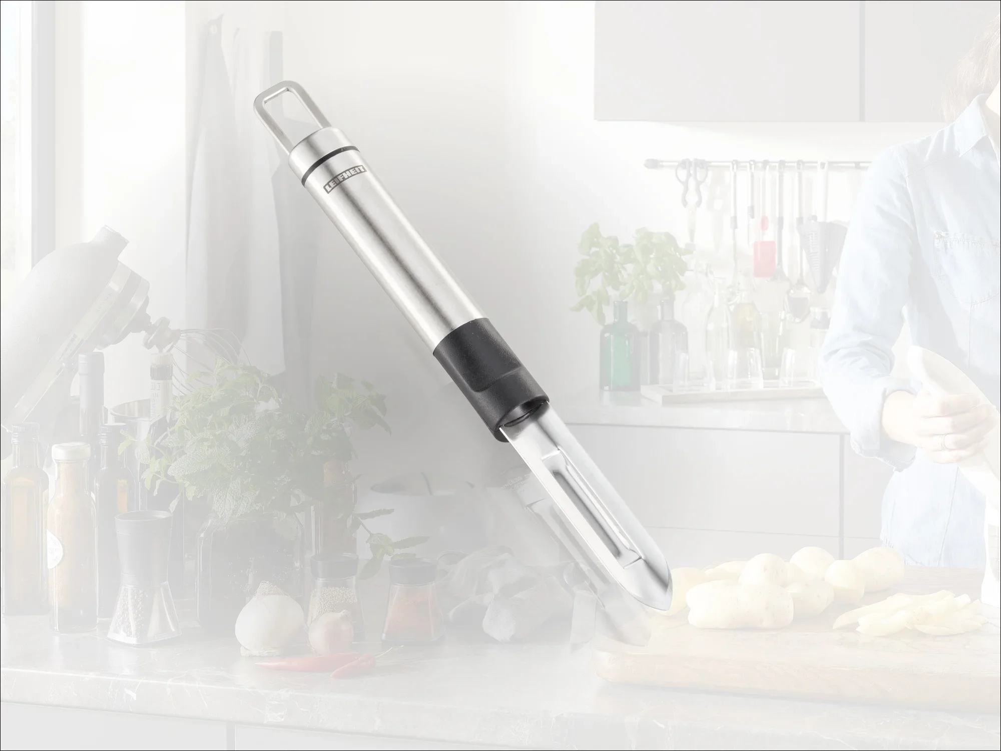 Wysokiej jakości obieraczka do warzyw ze stali nierdzewnej leży na blacie kuchennym. W tle widoczne są przybory kuchenne i świeże składniki. Idealna do precyzyjnego obierania.