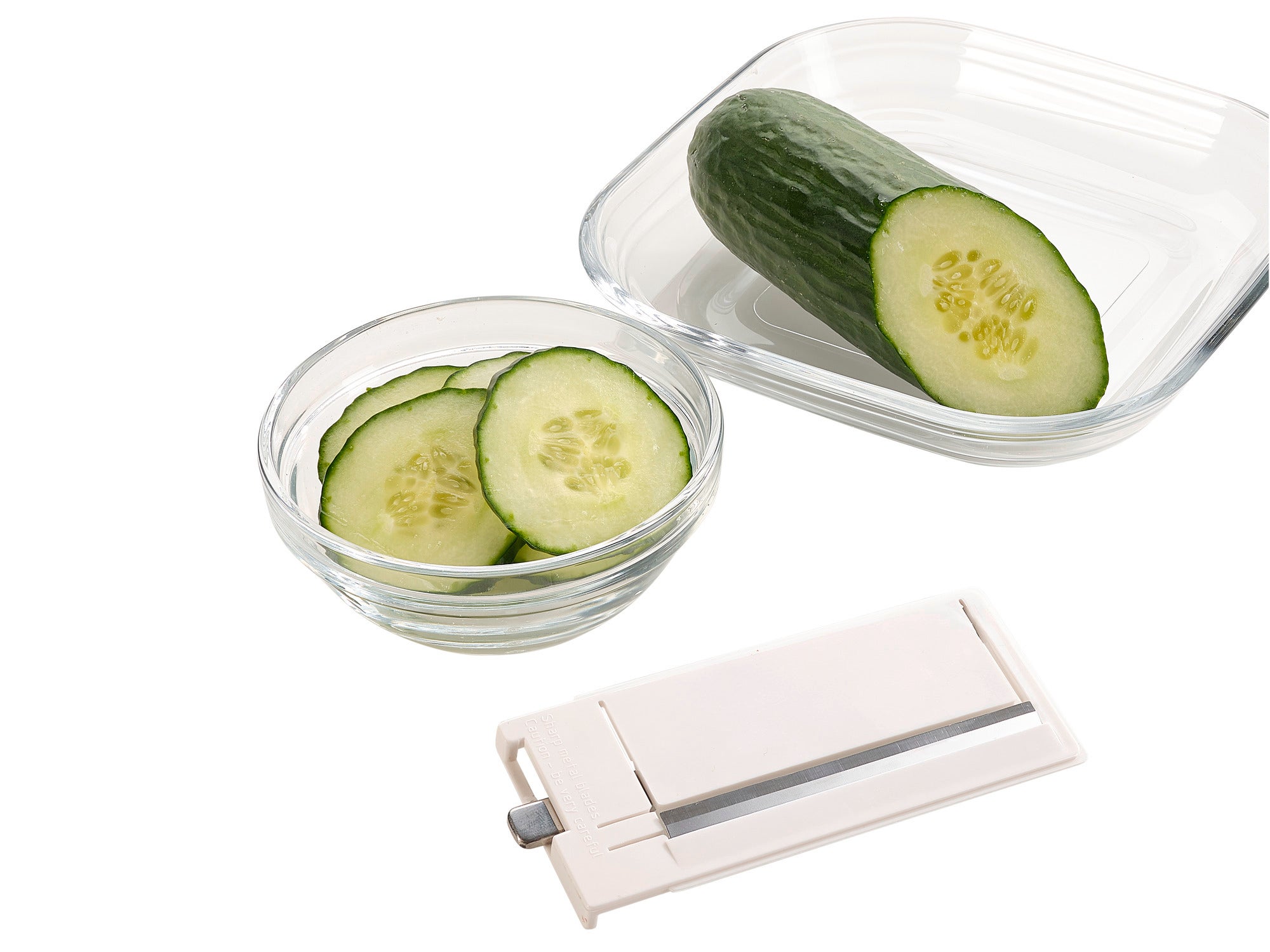 Une râpe multifonction 4+1 est posée à côté d'un bol contenant des tranches de concombre et un demi-concombre. Idéale pour couper rapidement et précisément les légumes.