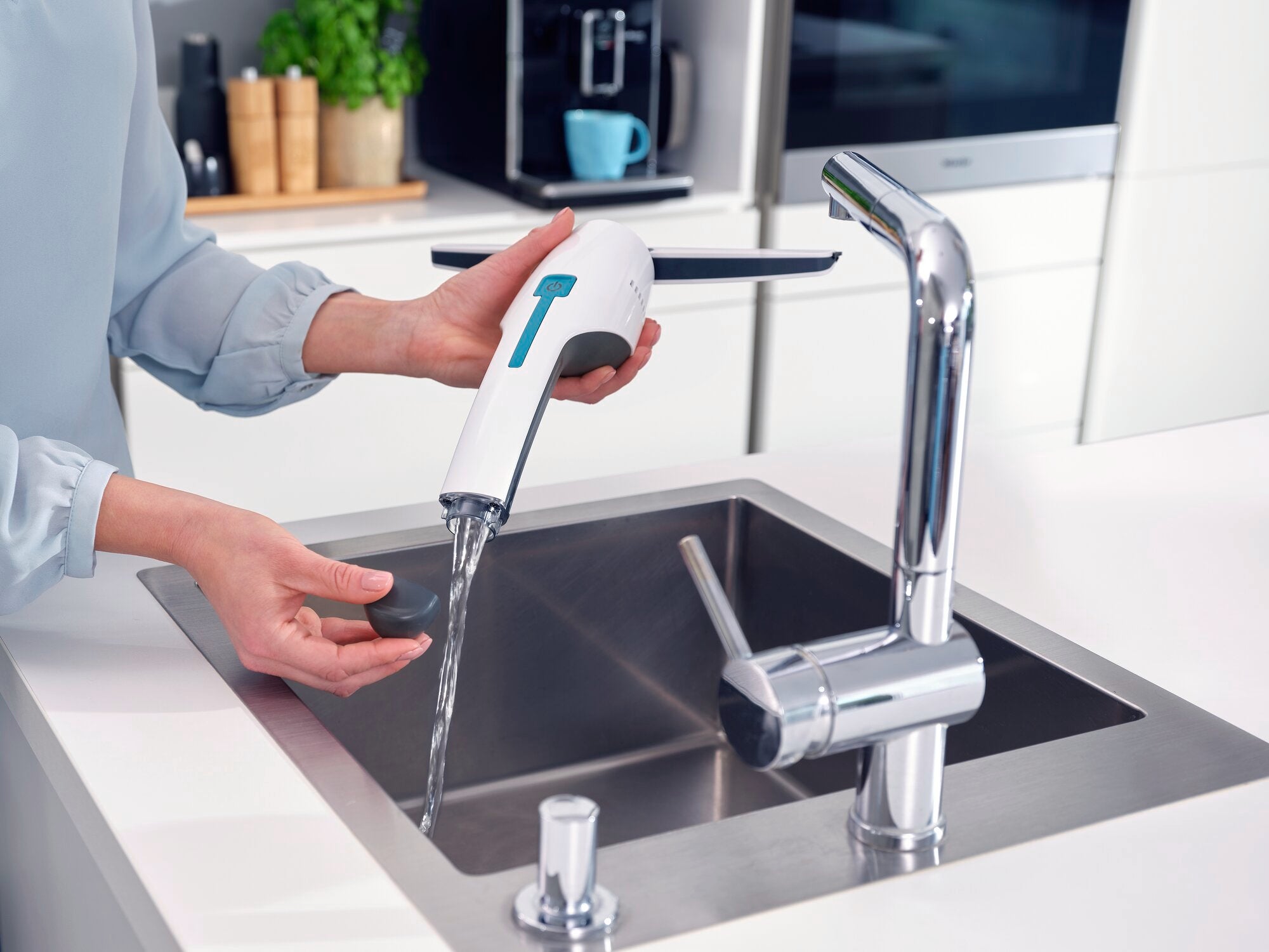 Una persona pulisce l'aspirapolvere per finestre Nemo sotto l'acqua corrente in una cucina moderna. L'aspirapolvere ha un corpo bianco con dettagli blu.