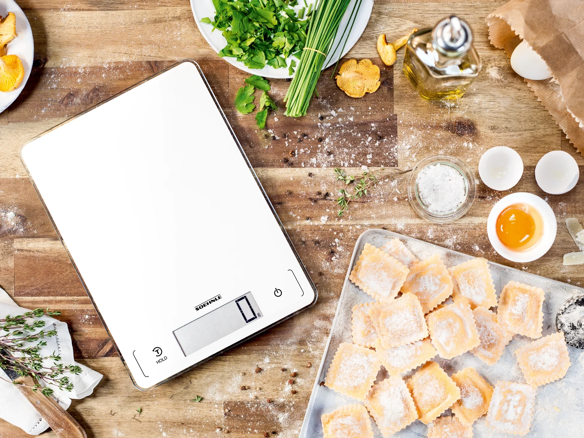 Digitale Küchenwaage Page Profi 300 auf einem Holztisch, umgeben von frischen Zutaten wie Kräutern, Eiern und Teigwaren. Perfekt für präzises Kochen und Backen.