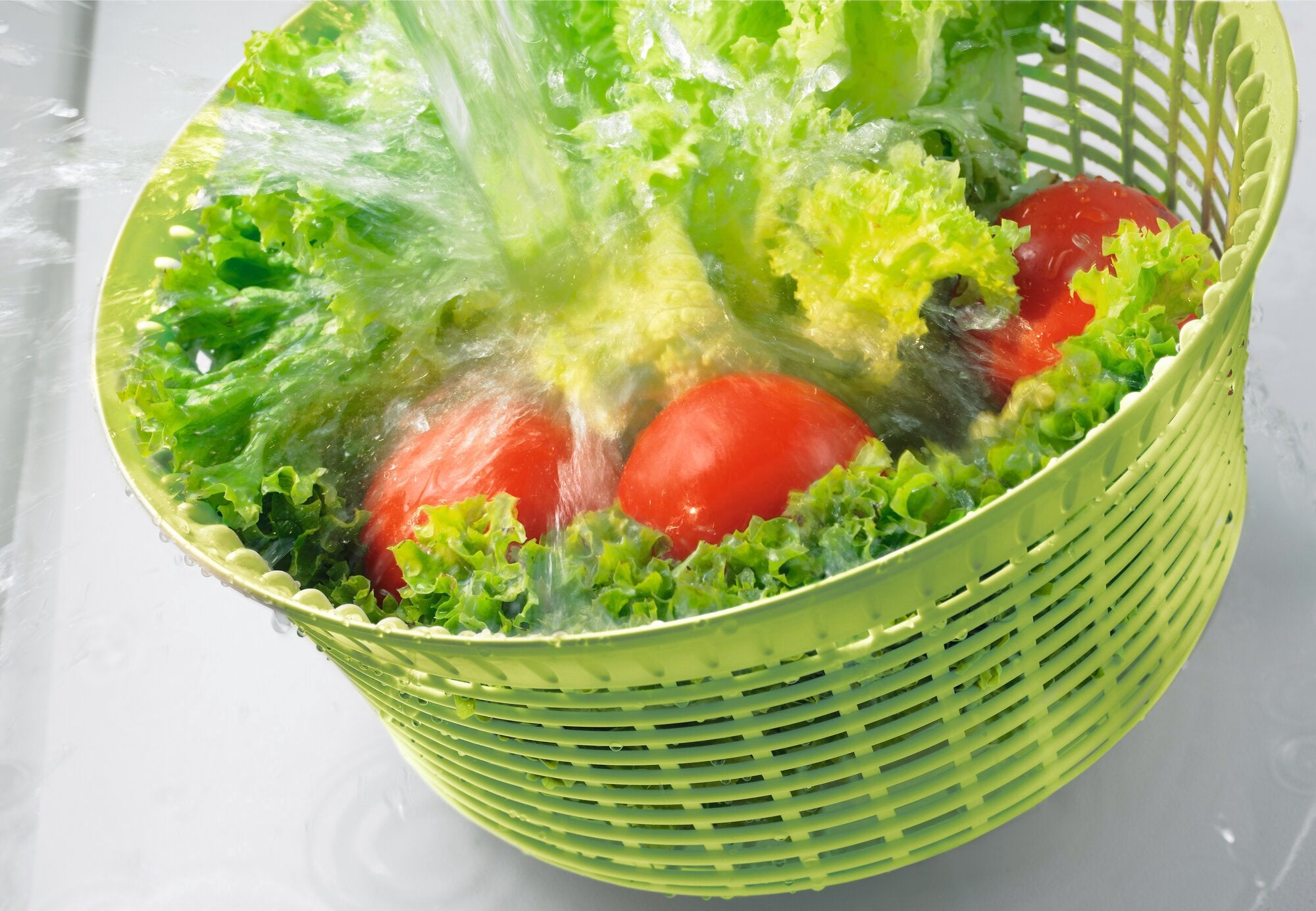 Salatschleuder 5,5l in Aktion: Frischer Salat und Tomaten werden in einem grünen Korb mit Wasser gewaschen. Ideal zum schnellen und effizienten Trocknen von Salat.