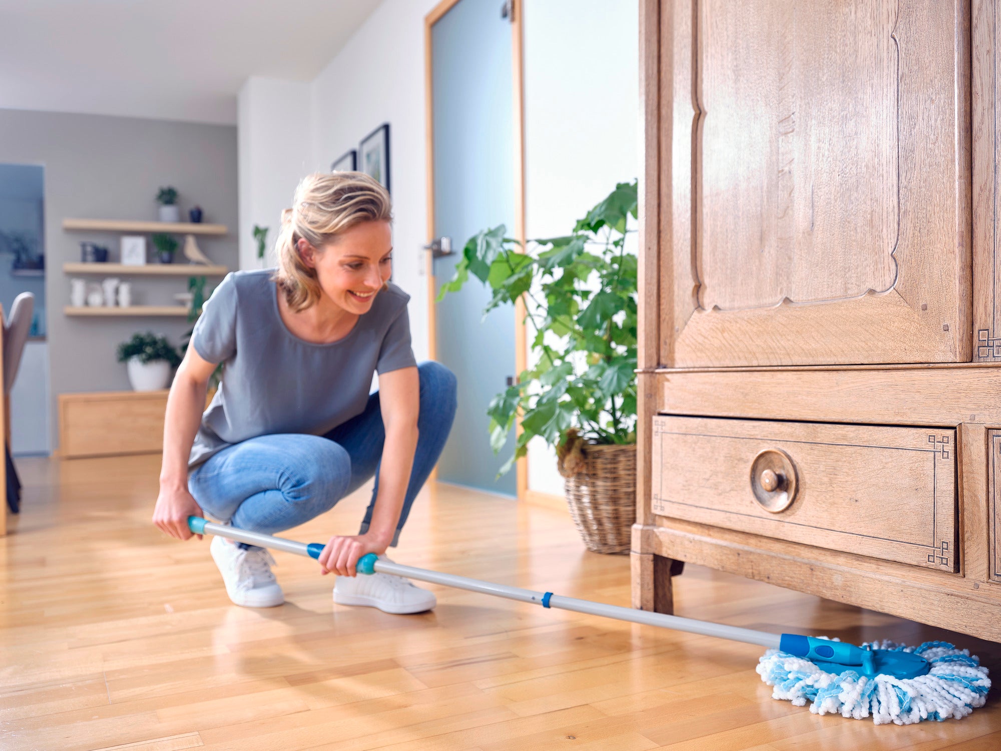 Une femme nettoie le sol en bois avec la serpillière CLEAN TWIST Ergo. La serpillière atteint sans effort les endroits difficiles d'accès sous les meubles. Idéal pour un nettoyage en profondeur et facile.
