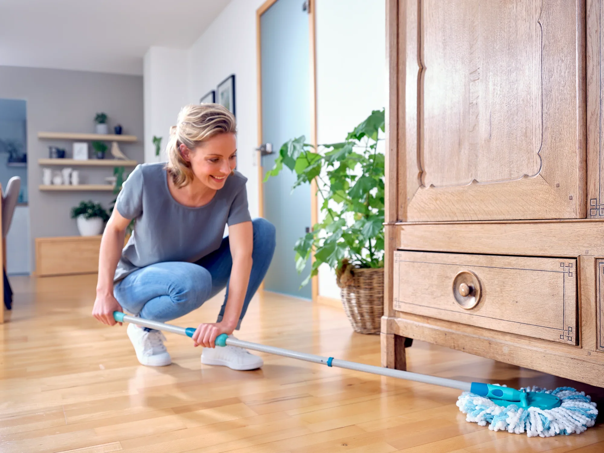 Una mujer limpia el suelo de madera con la mopa CLEAN TWIST Ergo. La mopa llega sin esfuerzo a los lugares de difícil acceso debajo de los muebles. Ideal para una limpieza profunda y sencilla.