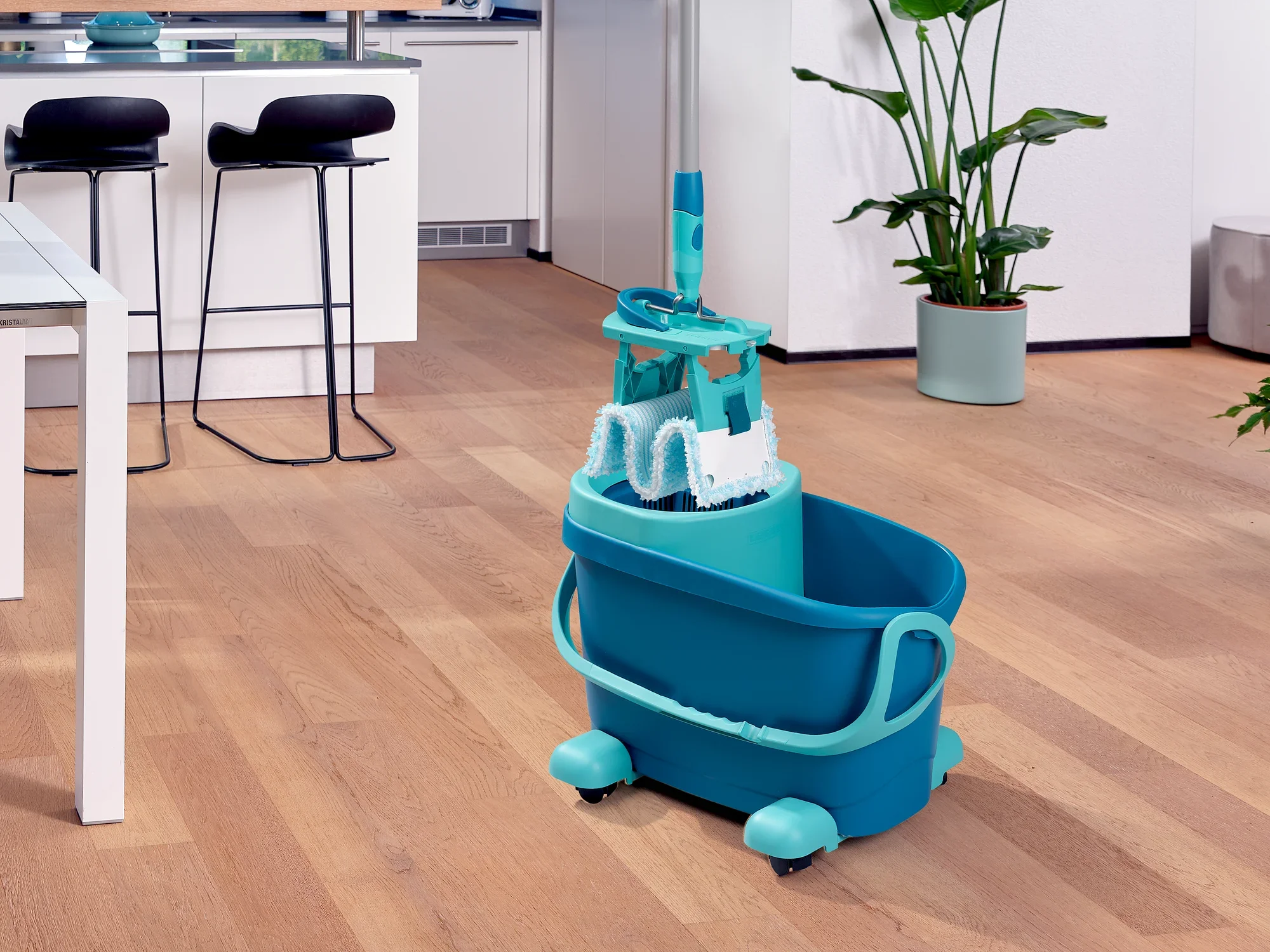 Een CLEAN TWIST M Ergo Set staat op een houten vloer in een moderne keuken. De emmer is uitgerust met een praktische trolley, ideaal om moeiteloos grote oppervlakken schoon te maken.