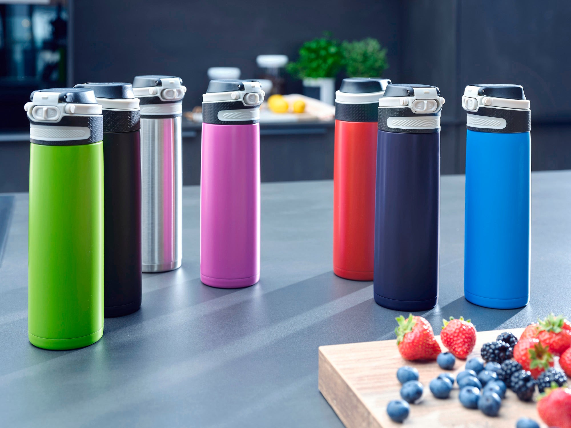 Flip insulated mug 600 ml in various colours on a modern kitchen worktop. Fresh berries on a wooden board can be seen in the foreground. Ideal for on the go.
