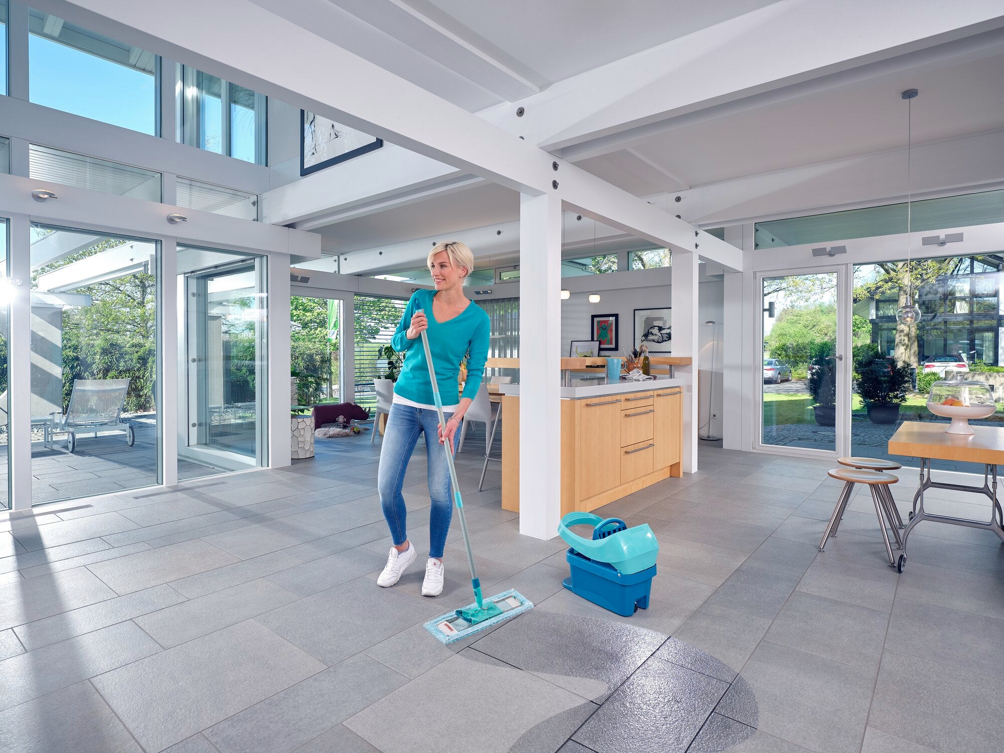 Een vrouw dweilt de vloer van een moderne, lichtdoorstroomde kamer met de Profi XL dweilmop. De mop heeft een superzachte hoes, ideaal voor kwetsbare oppervlakken.