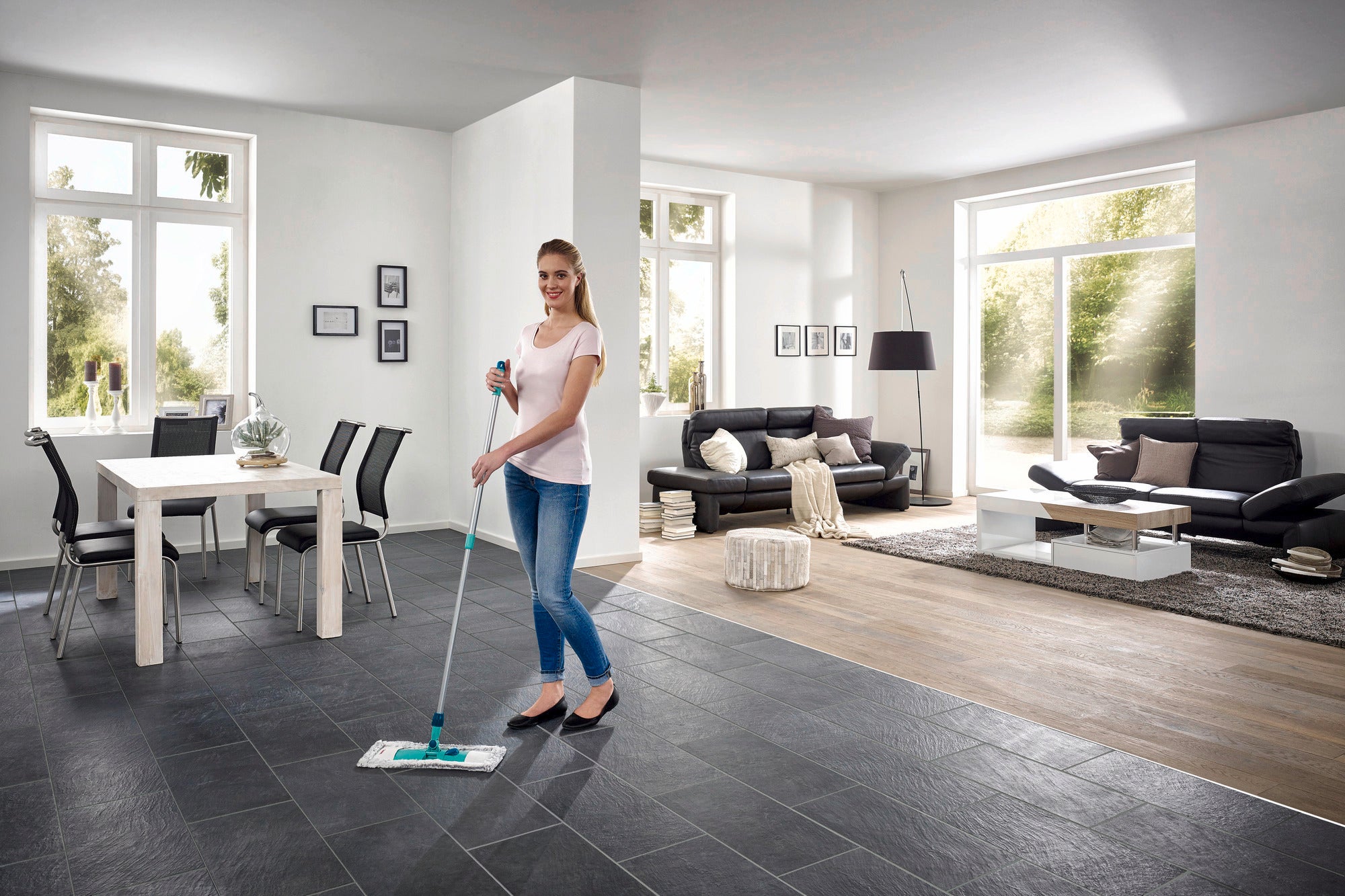 Een vrouw dweilt de vloer in een moderne woonkamer met de Classic dweilmop. De kamer is licht en stijlvol, met grote ramen en elegante meubels.