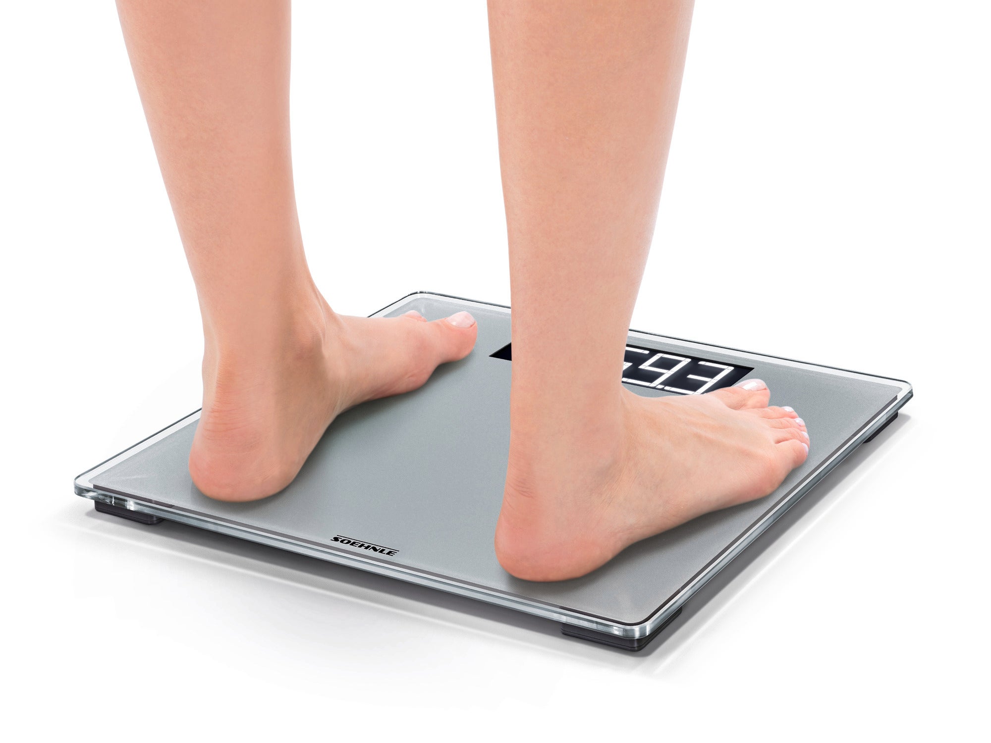 A person is standing barefoot on the Style Sense Comfort 600 digital bathroom scale. The scale shows the weight on a clear, easy-to-read display.
