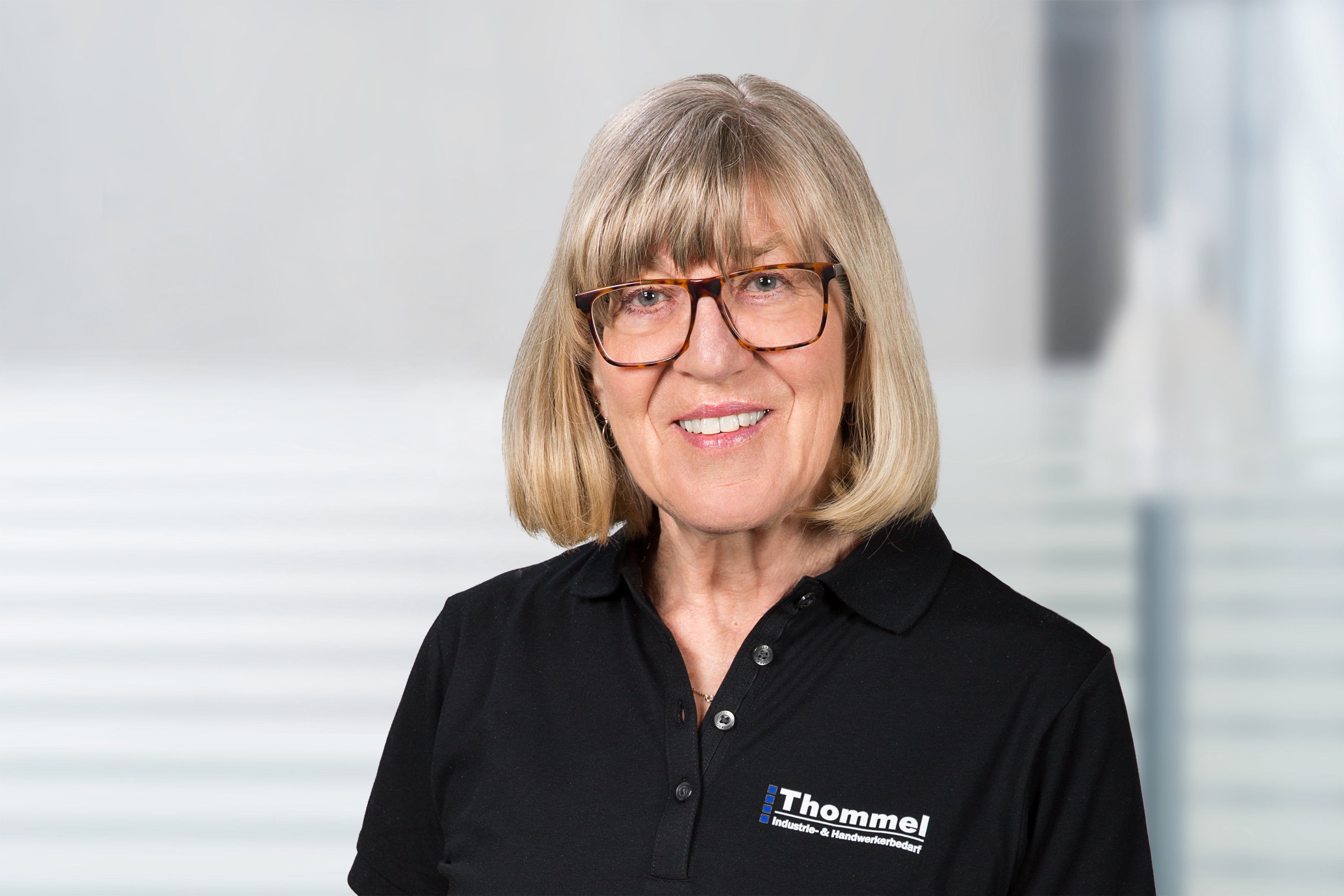 person, glasses, blonde hair, black polo, logo