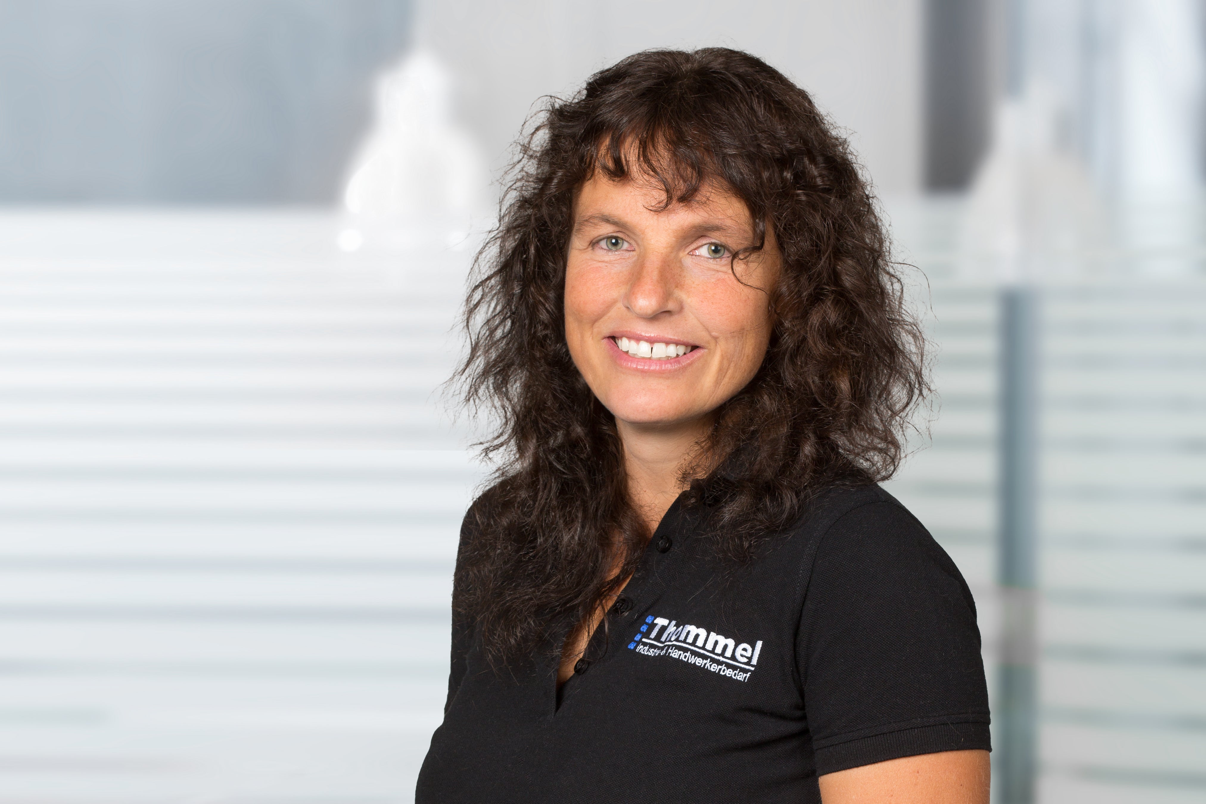 frau, schwarz polo, lockige haare, blaues logo, polo mit brusttasche
