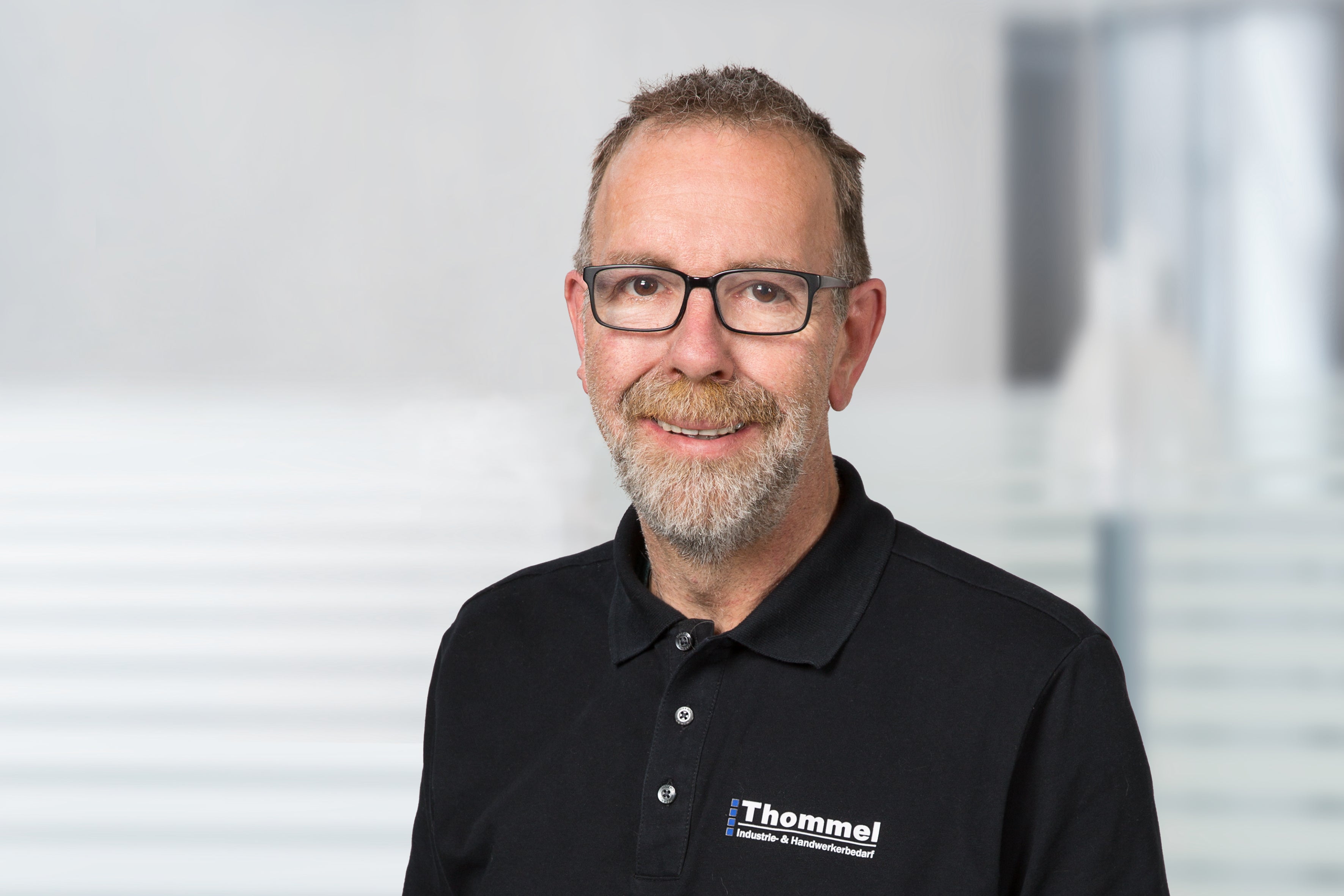 Mann, Brille, Bart, schwarzes Polohemd, Logo