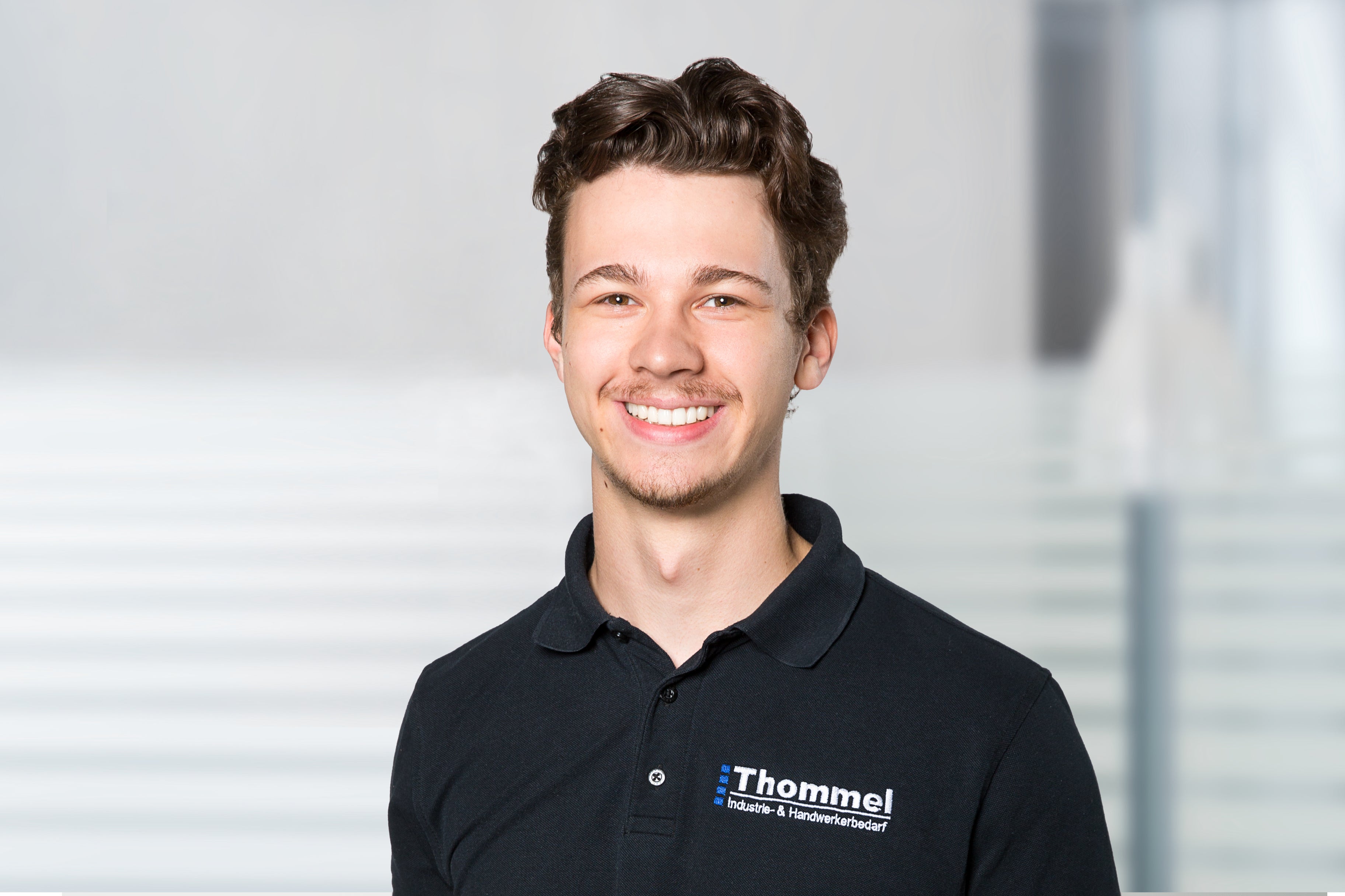 Portrait, junger Mann, schwarzes Polohemd, Lächeln, Mitarbeiteruniform