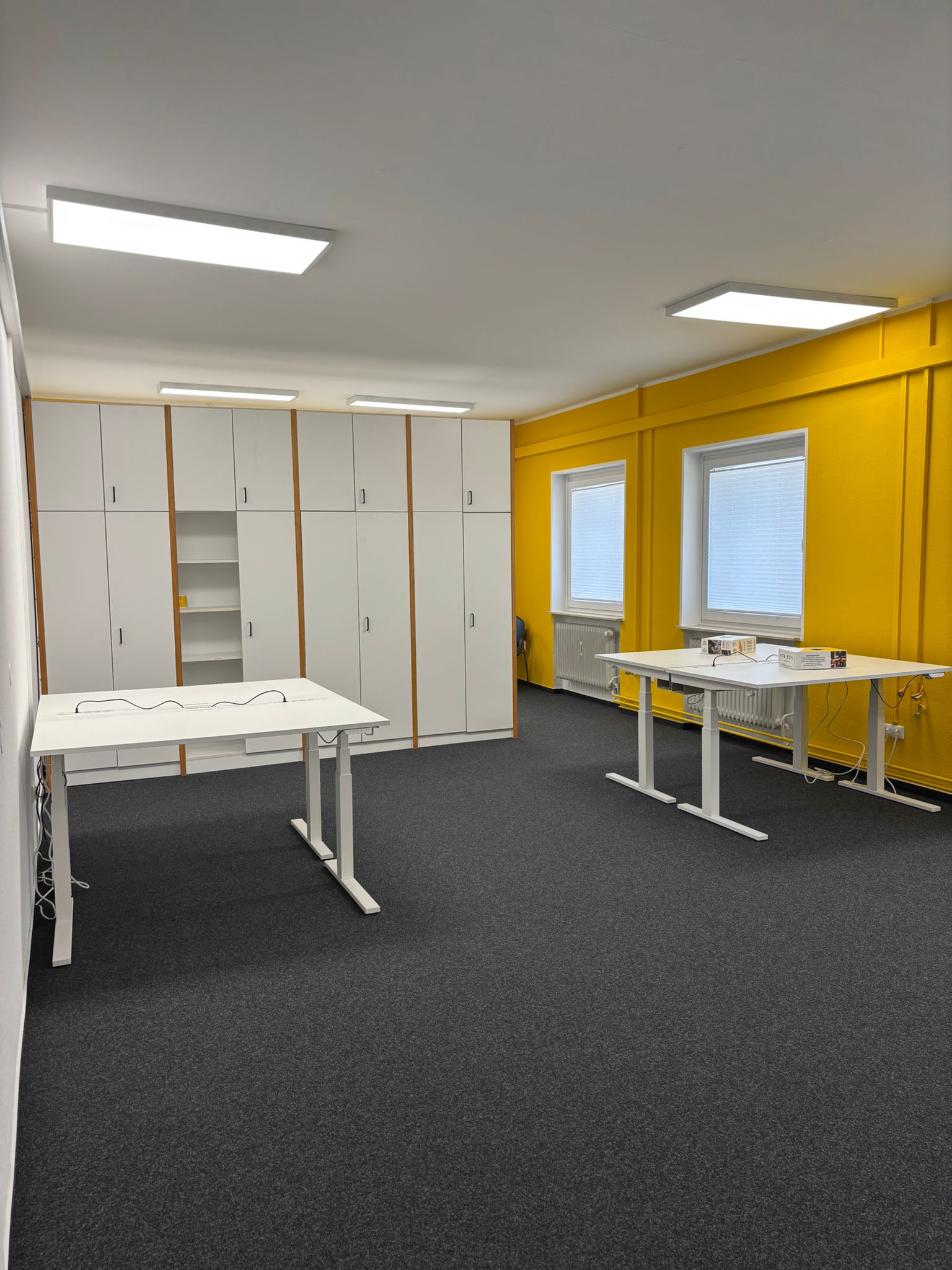 Frische Farben für frische Ideen und frischen Wind im SIMPEX Büro. Weiß und gelbe Wände und ein dunkel grauer Fußboden mit weißen höhenverstellbaren Schreibtischen und einer weißen Schrankwand