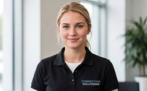 Eine professionelle Service-Mitarbeiterin in einem modernen Büro, die ein schwarzes Poloshirt mit dem gestickten Connective Solutions-Logo trägt